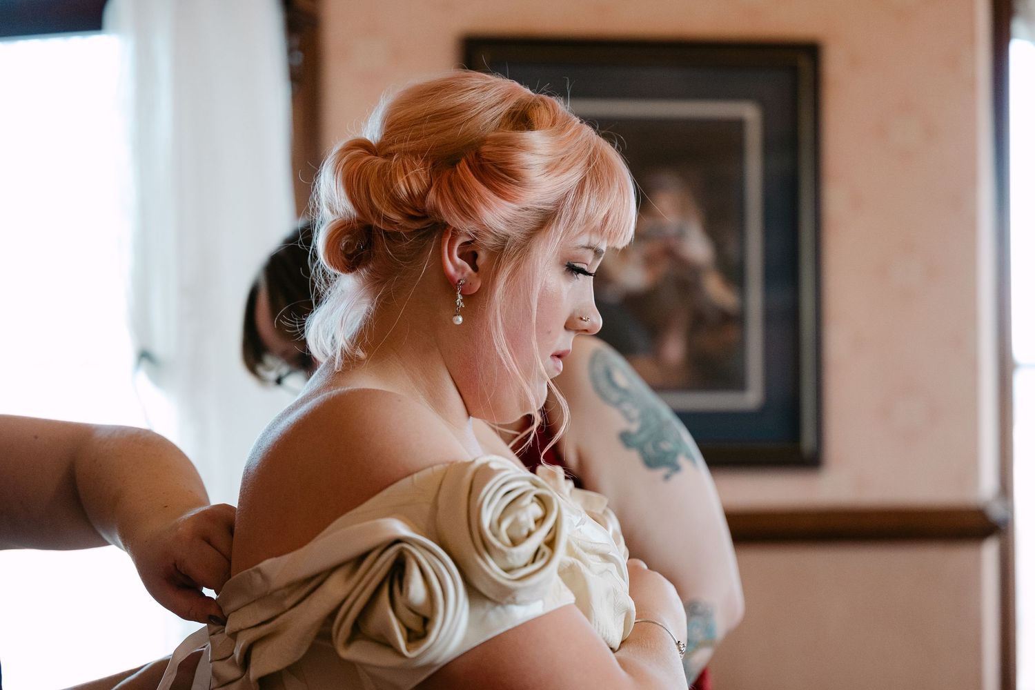 Central MN Wedding Photos | Bride with red updo hairstyle getting her dress fastened before wedding ceremony.