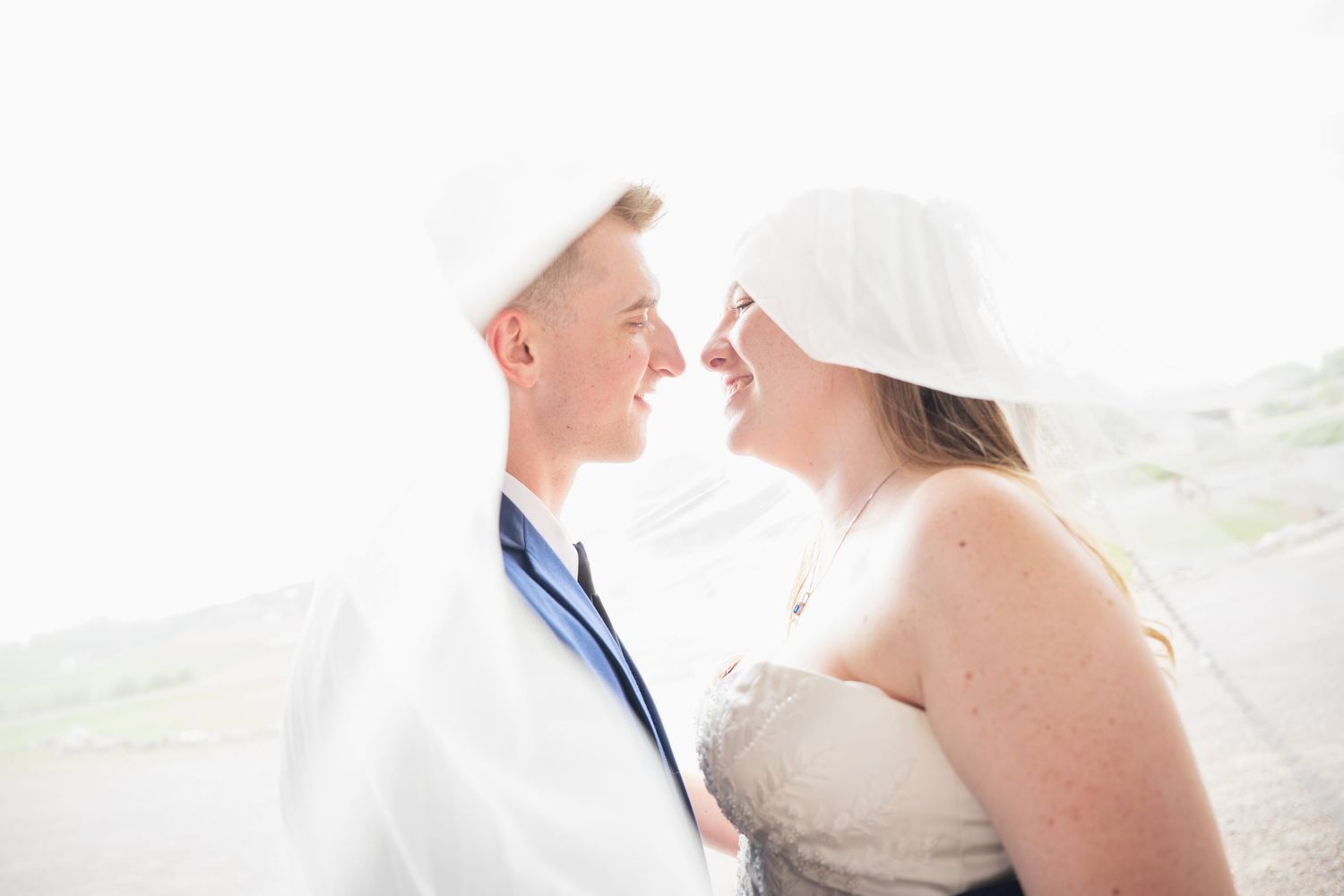 Romantic couple shares an intimate moment under a white veil during their outdoor wedding ceremony at Northern Lights near Milaca MN..