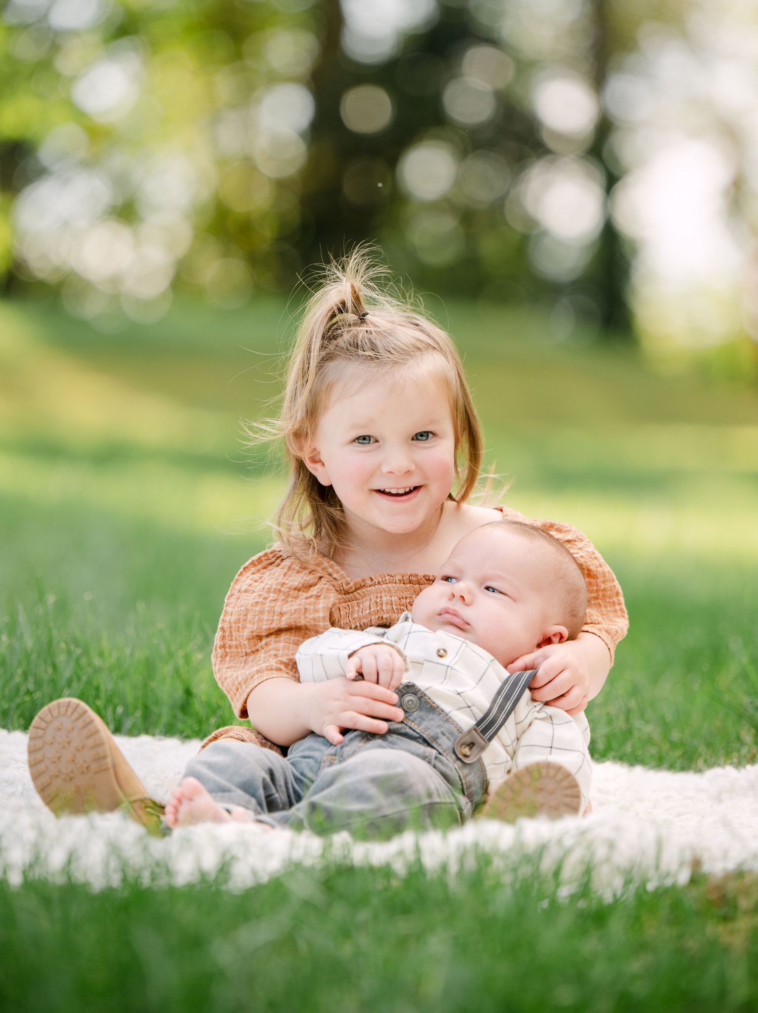 A series of three connected photos showing two young children lying on a blanket in the grass on a sunny day.
