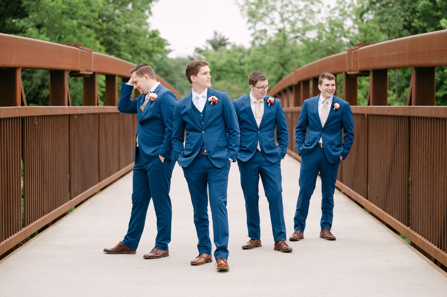 Wedding party wearing navy suits walking across a wooden bridge.