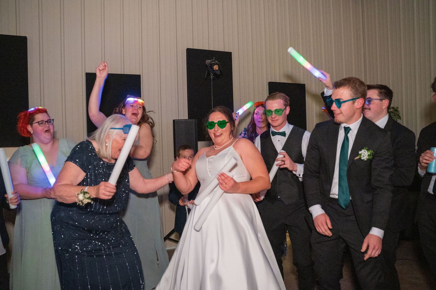 Wedding reception party guests dancing with colorful light-up glow sticks in a dark venue.