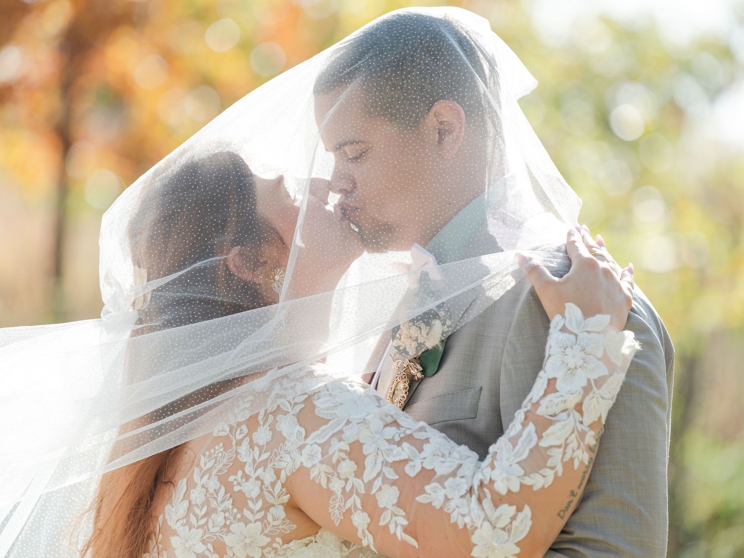 Romantic couple embraces and kisses in a dreamy autumn setting with golden leaves and sunlight filtering through trees.