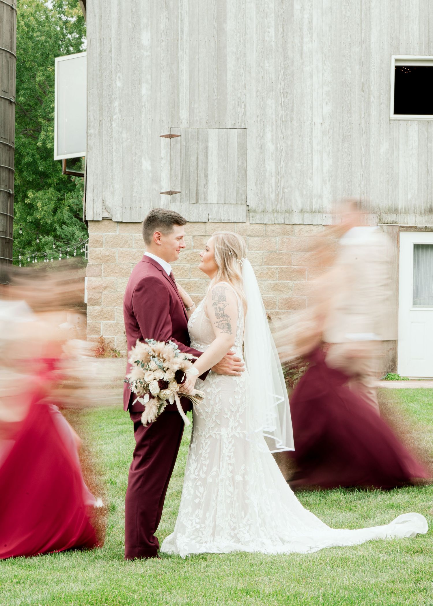 Wedding party poses for dynamic motion shots in front of rustic barn with burgundy bridesmaids dresses.