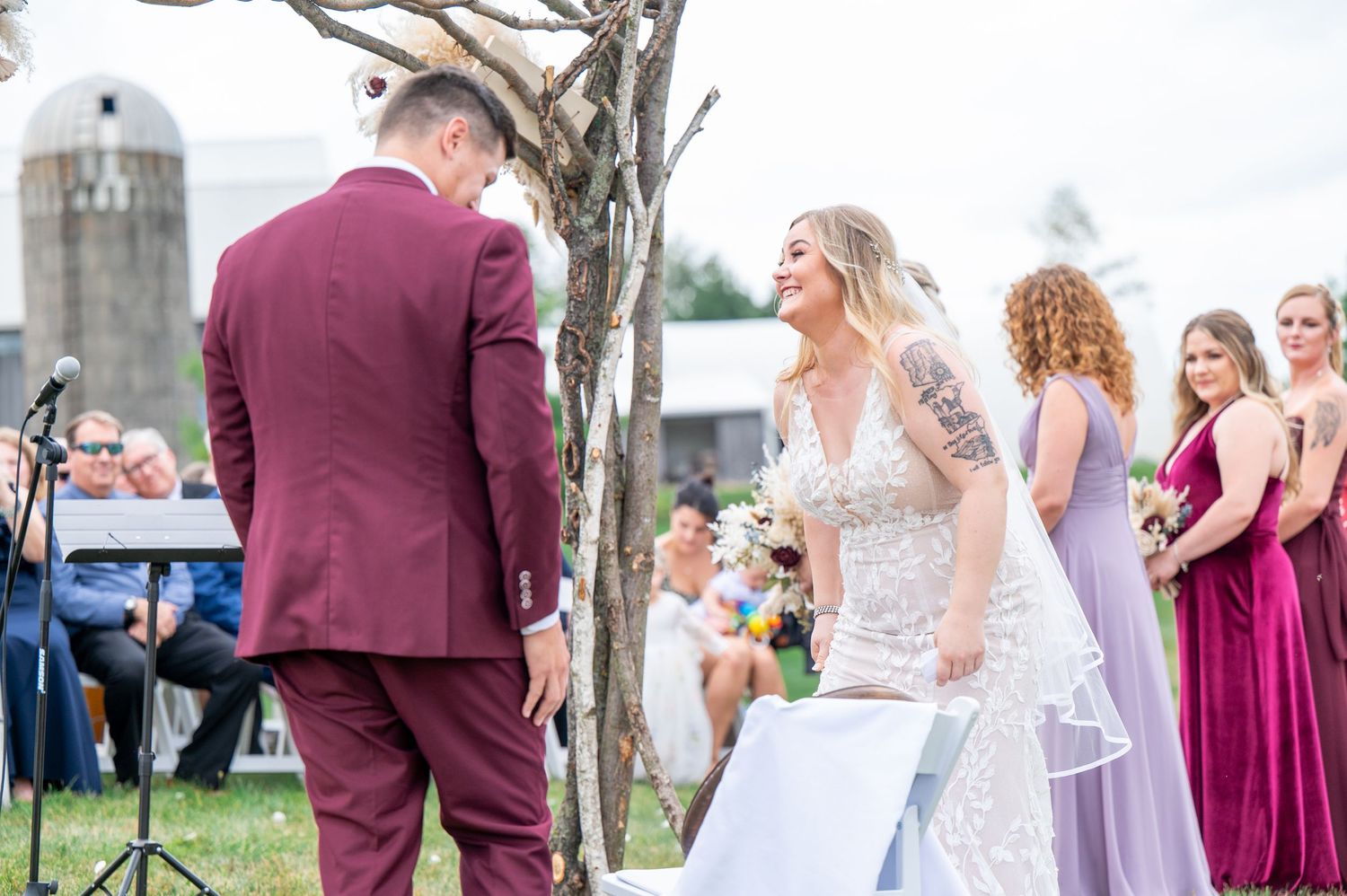 Wedding party members in burgundy and ivory attire pose together in front of rustic outdoor scenery.