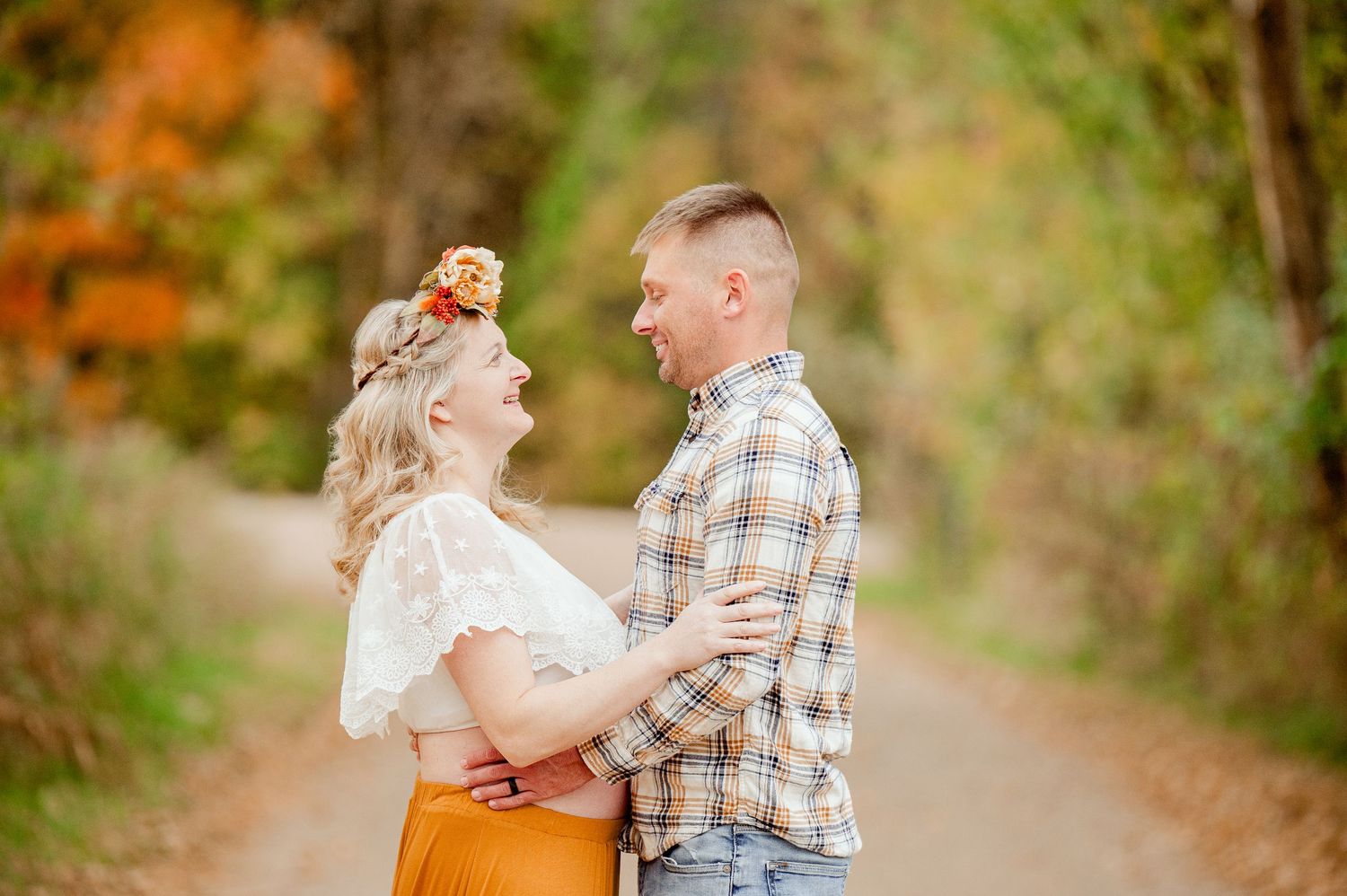 Happy couple laughing and embracing on autumn tree-lined path with vibrant fall foliage in background.