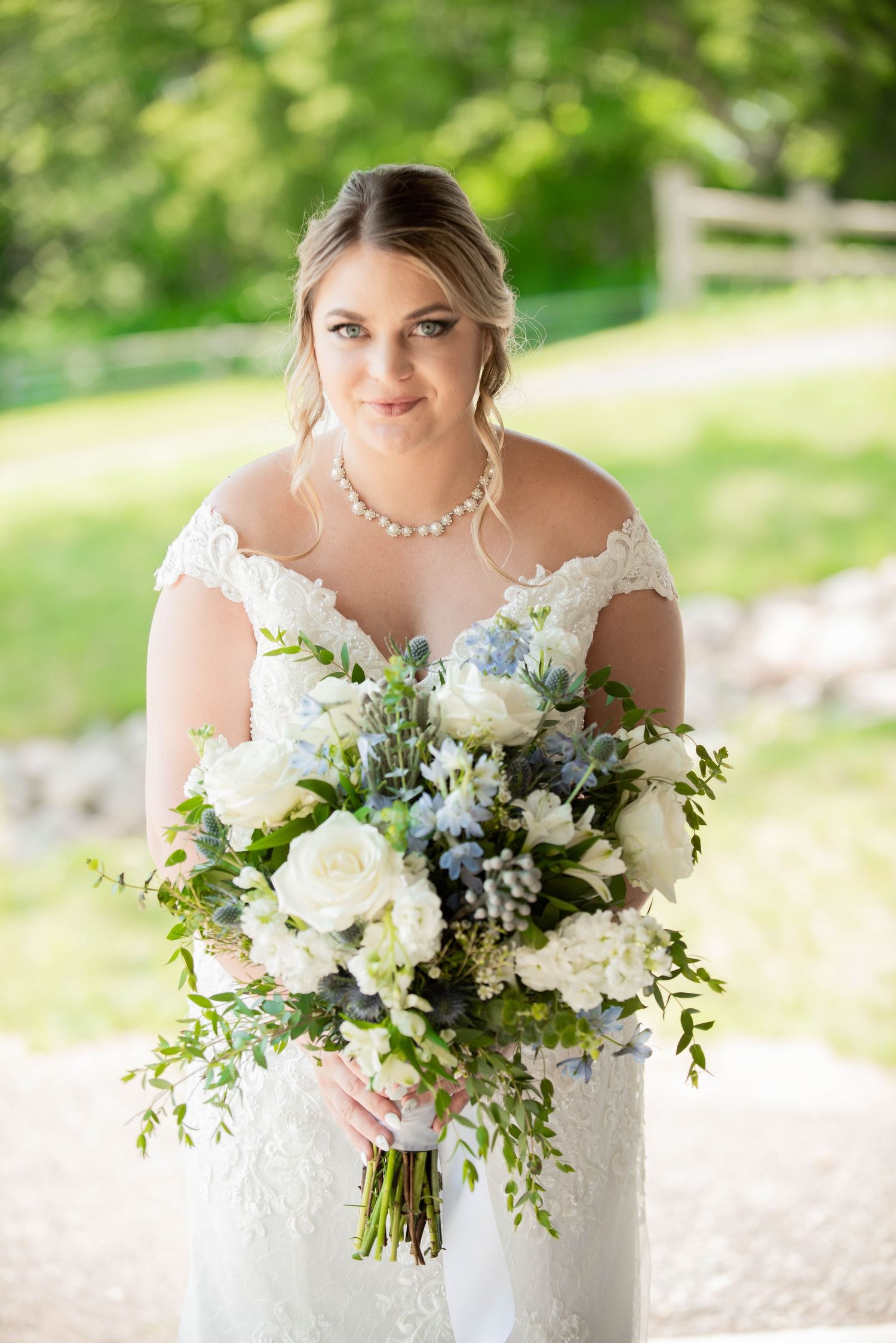 A wedding bouquet features white roses and cascading greenery with delicate blue accents. Zimmerman MN Weddings