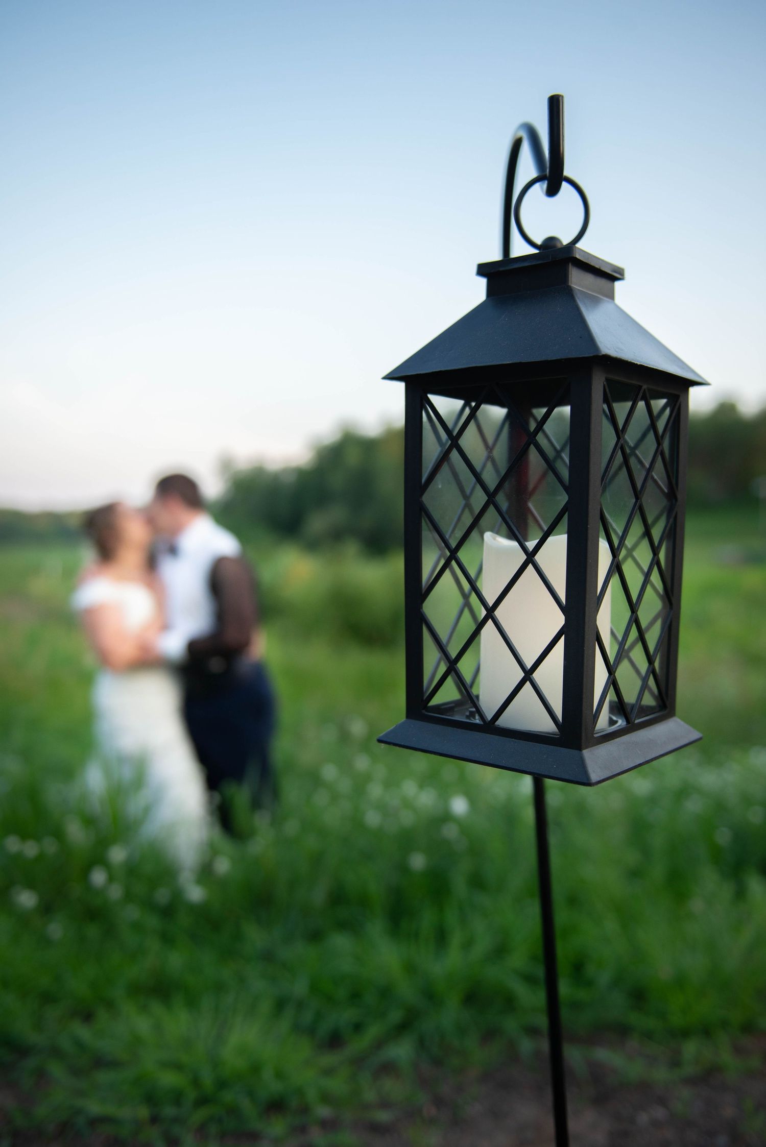 A decorative black lantern in the foreground with a blurred outdoor wedding scene in the background. Zimmerman MN Weddings