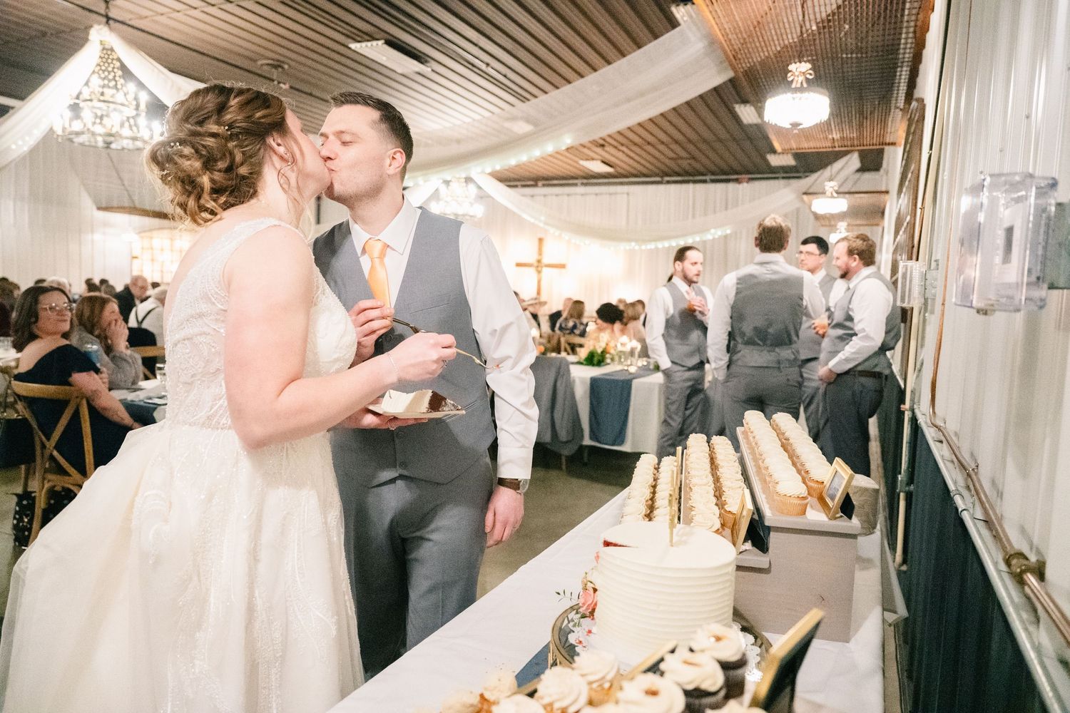 Bride and groom share a kiss at the dessert table during their wedding reception.