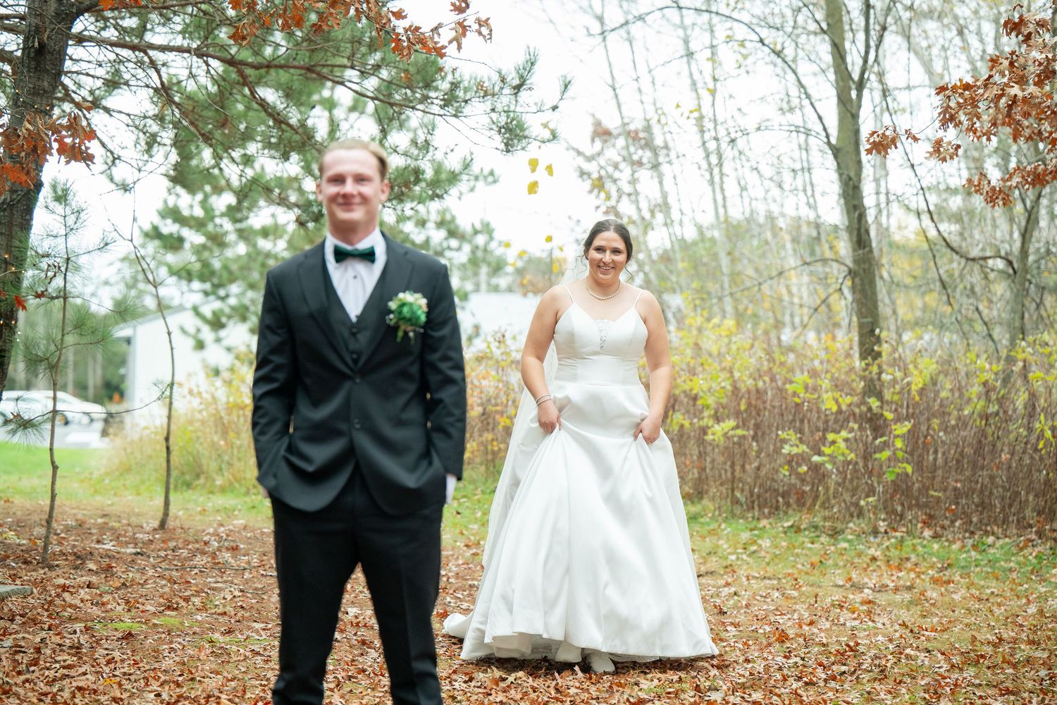 Bride and groom share a romantic moment in a wooded area with autumn foliage.