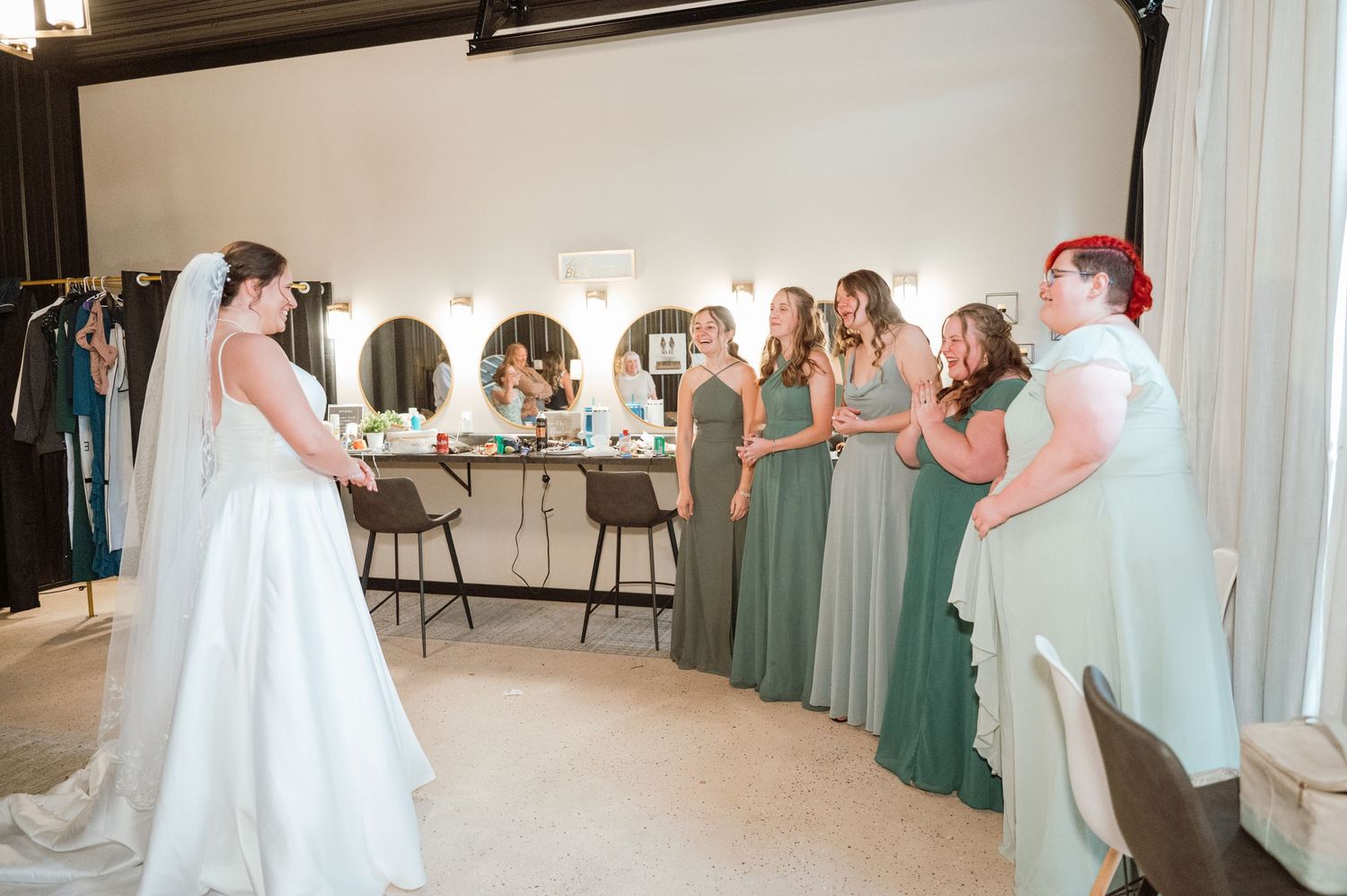 Wedding party members dance and celebrate together on a white dance floor at an indoor reception venue.
