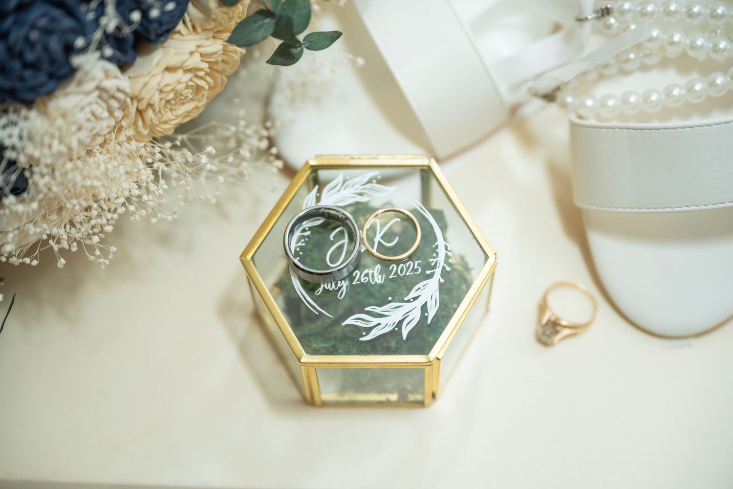 Gold wedding rings displayed in a geometric glass box with delicate pearl decorations at Northern Lights near Milaca MN..