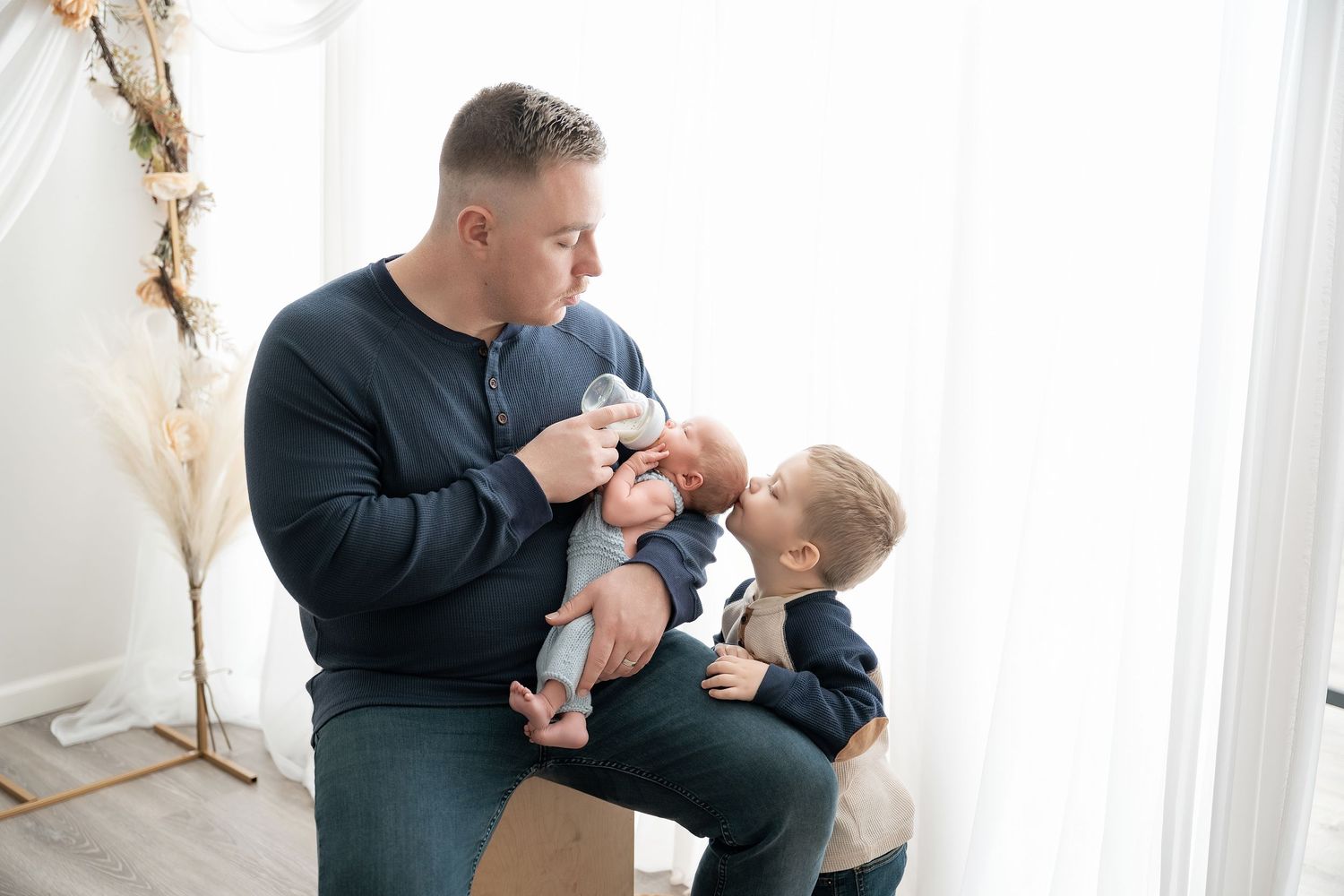Minnesota Best newborn photographer -  a Tender family moments captured in a bright white room with natural light streaming through windows.