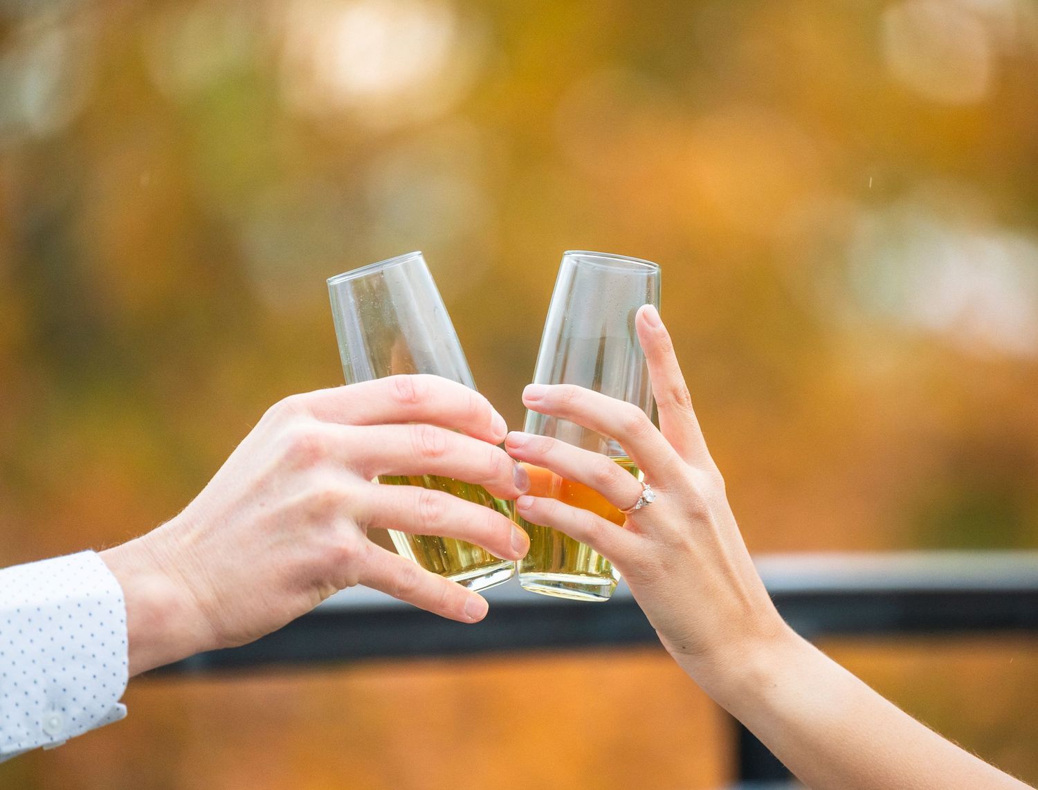 Engagement Photos in central Minnesota a Close-up of hands sharing a toast against a blurred autumn background.