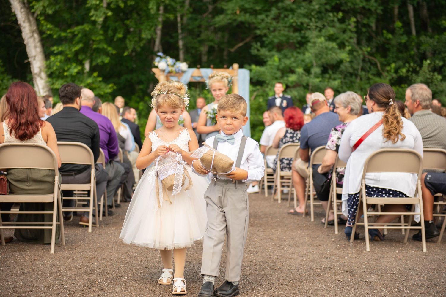 Two young attendants in formal wear walk down the outdoor ceremony aisle. Zimmerman MN Weddings