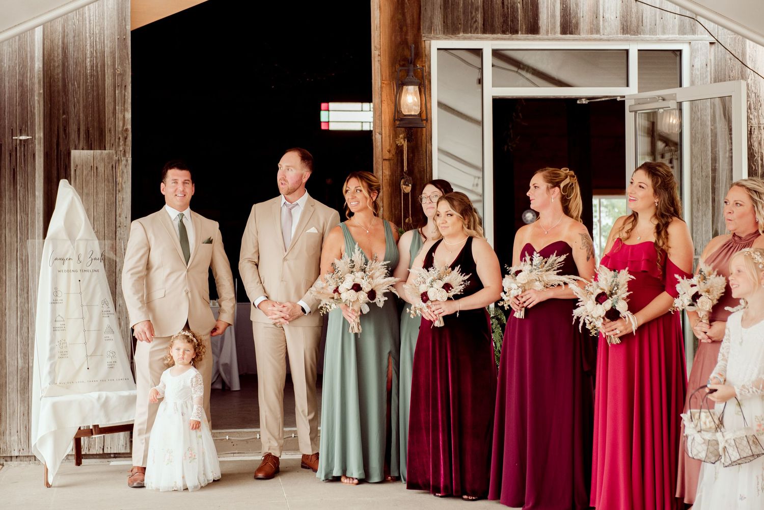 Wedding party poses together wearing burgundy and sage green dresses with light colored suits.