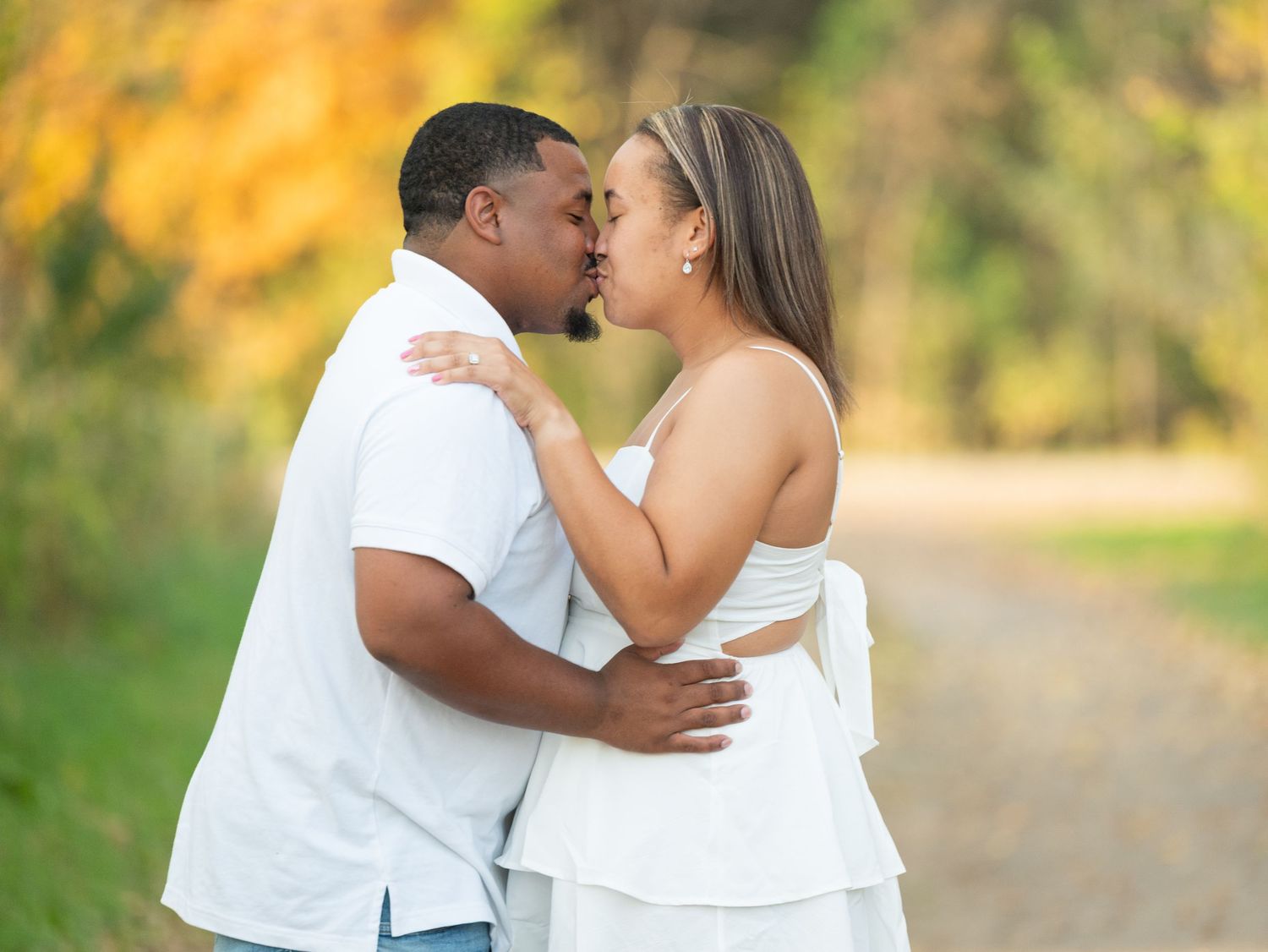 Central Minnesota Best Engagement Photographer - Couple sharing a romantic kiss outdoors on a dirt path surrounded by autumn foliage.