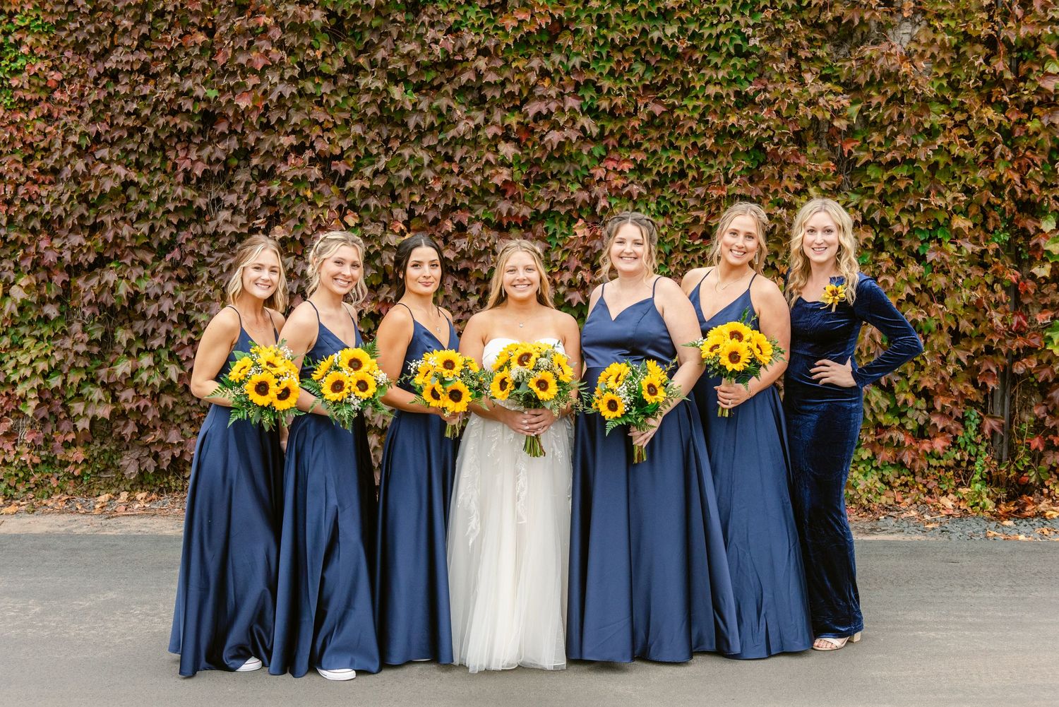 Central MN Wedding Photos | Bridesmaids in navy blue gowns holding sunflower bouquets posing with bride before wedding.