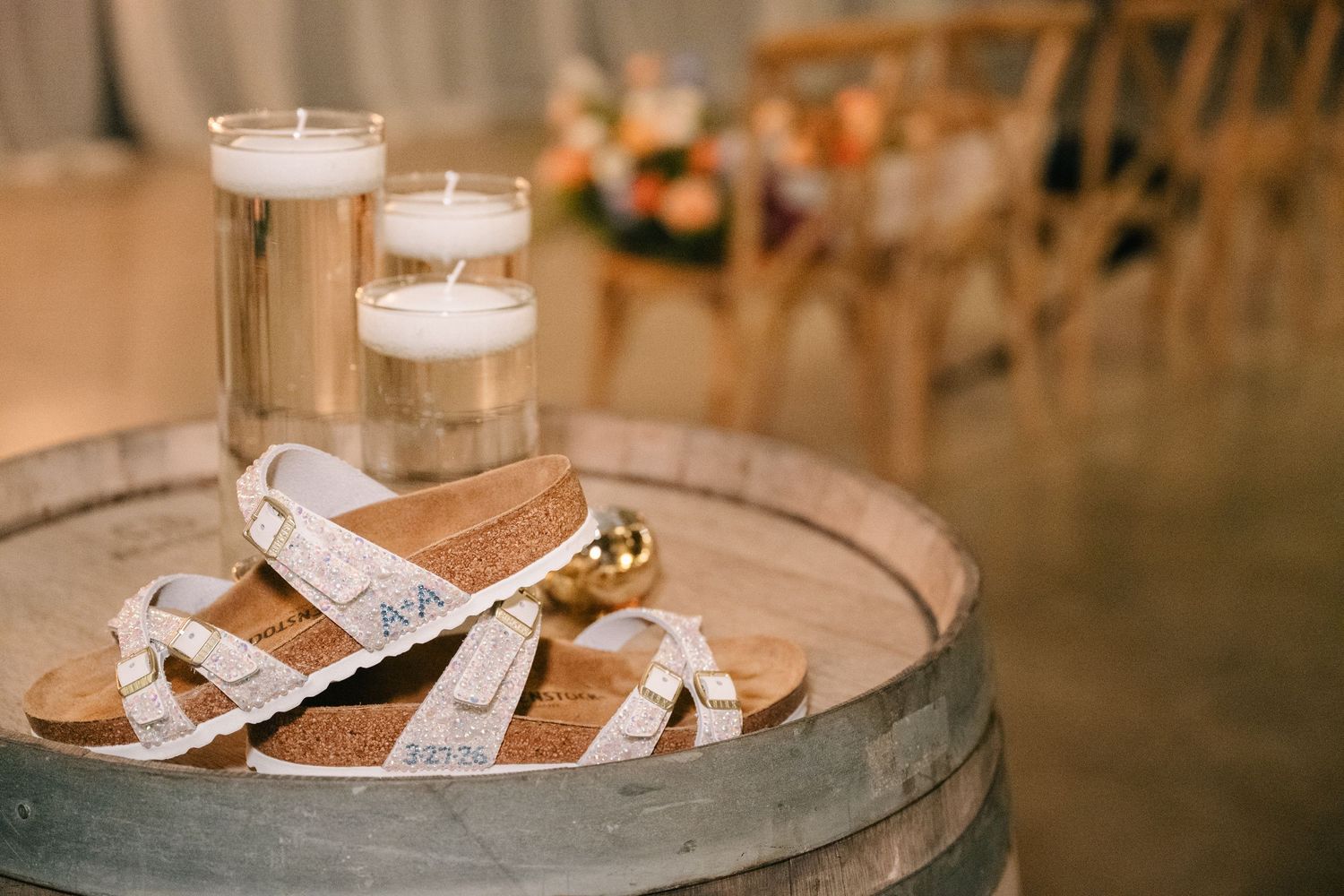 White lace bridal sandals on a rustic wine barrel with floating candles and floral decor at a wedding venue.