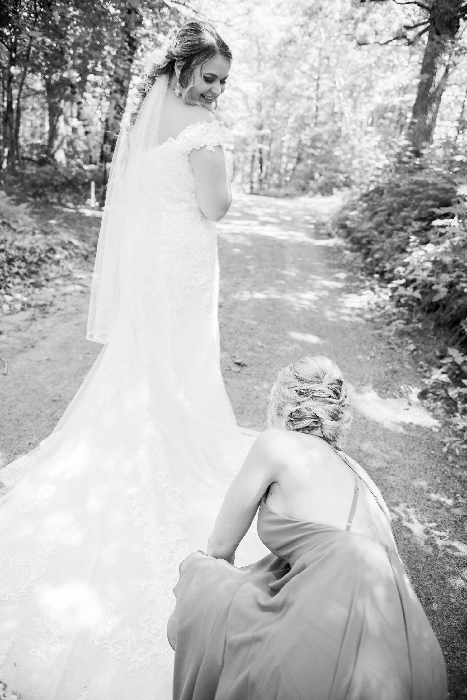 Black and white photo of wedding dress being adjusted on outdoor path. Zimmerman MN Weddings