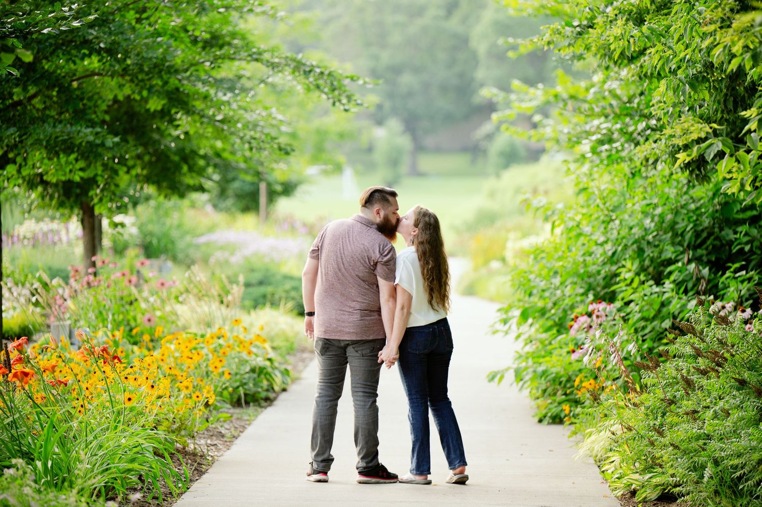 Couple walking together on garden path surrounded by vibrant flowers and lush greenery on summer day.