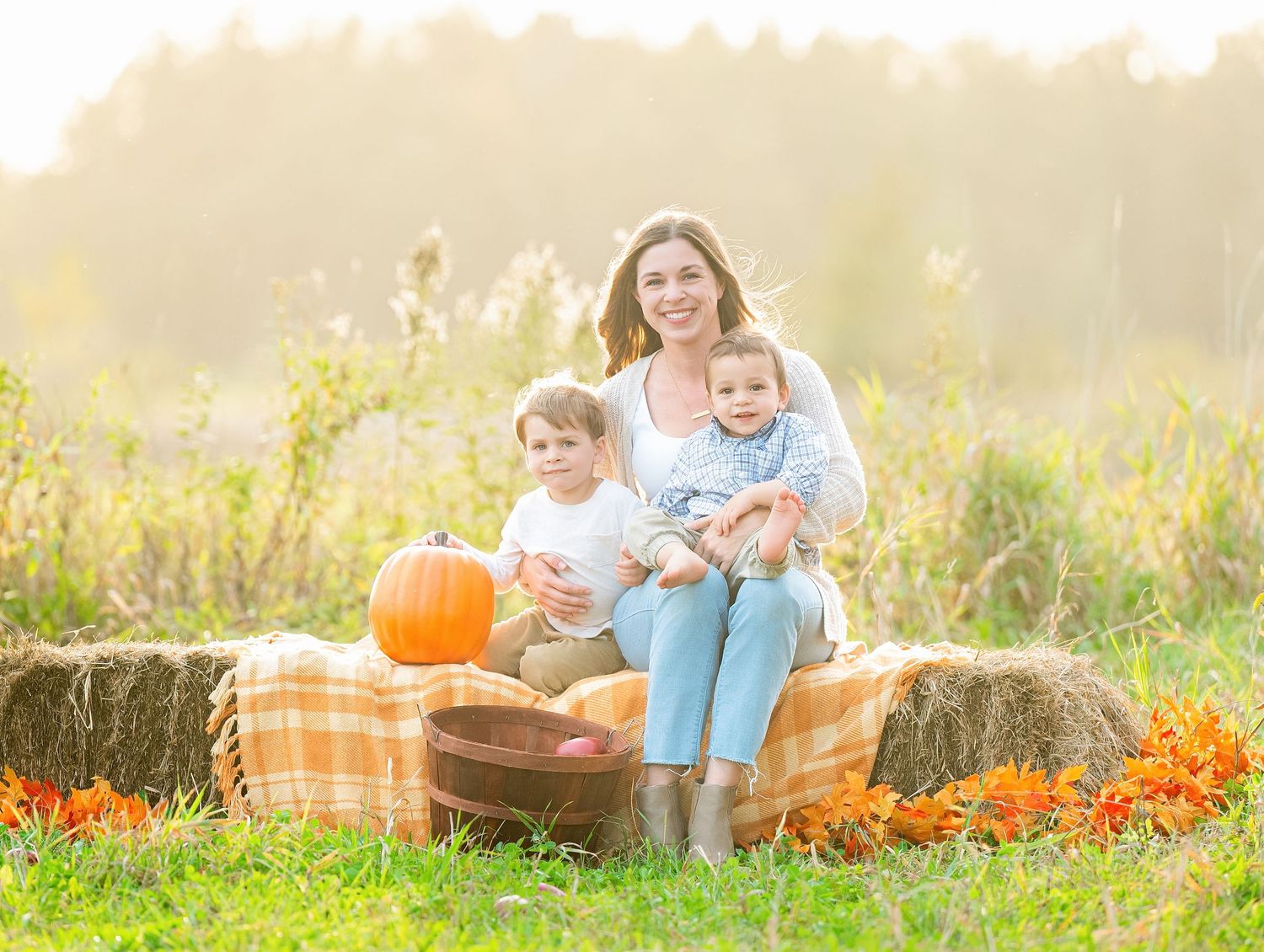 In central Minnesota a family sits together in a grassy field during golden hour with autumn pumpkins and fall decorations.