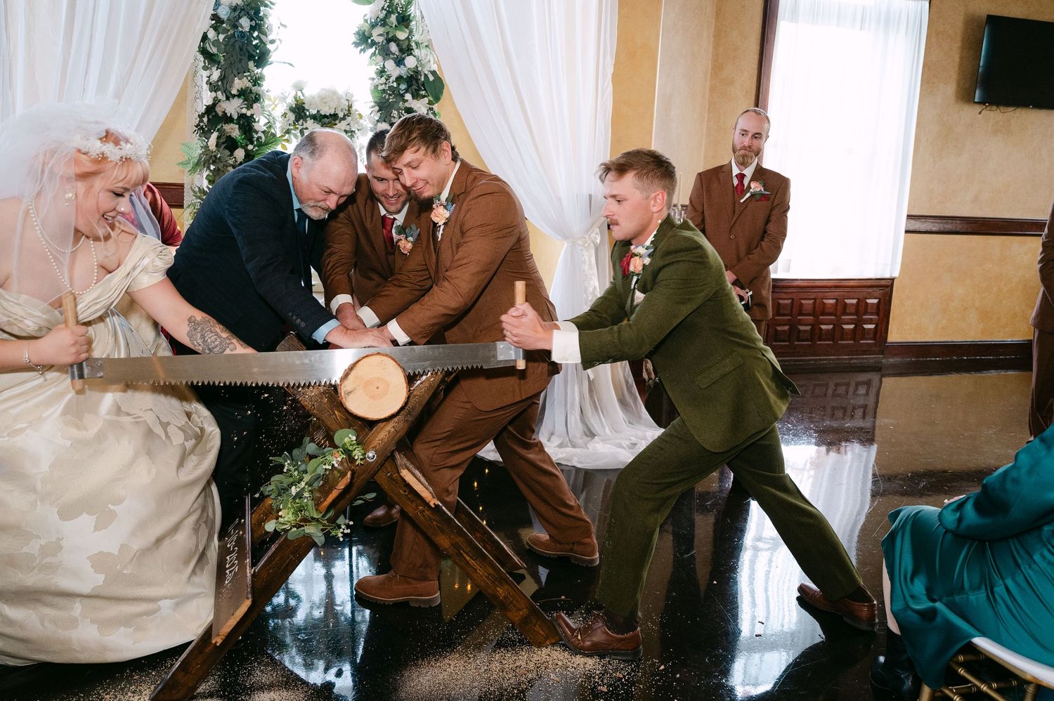 Central MN Wedding Photos | Wedding guests sawing log at rustic ceremony tradition with bride and groom in historic venue.