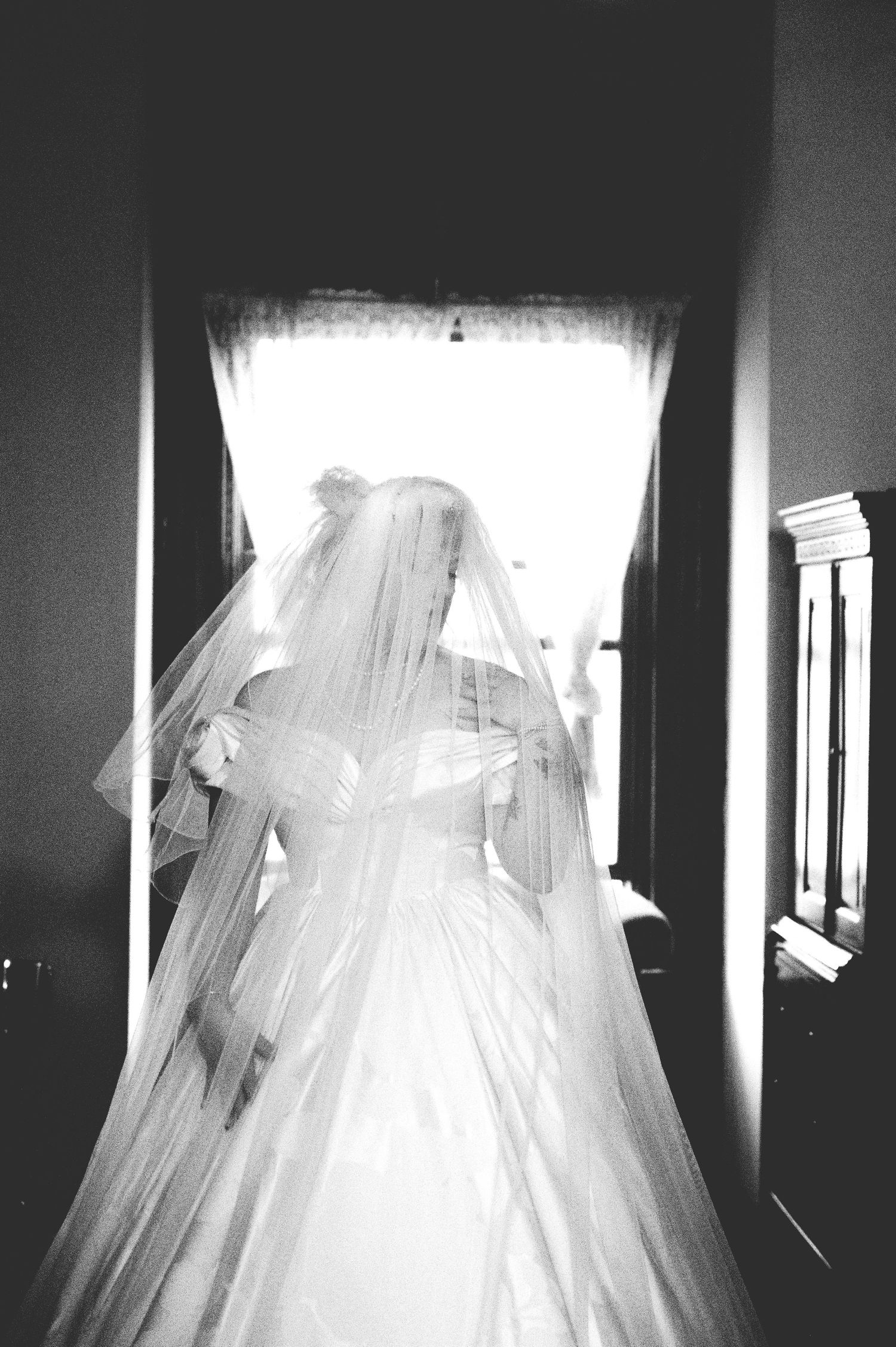 The Historic Concord Exchange Black and white photo of a bride in a flowing gown and veil standing in a hallway backlit by a bright window.