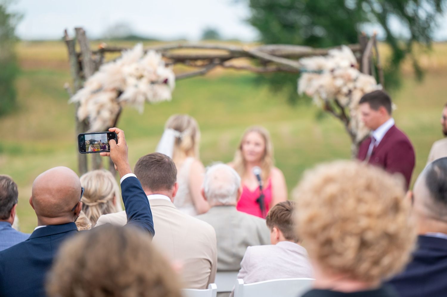 A wedding ceremony scene showing seated guests in an outdoor setting with natural greenery and decorations.