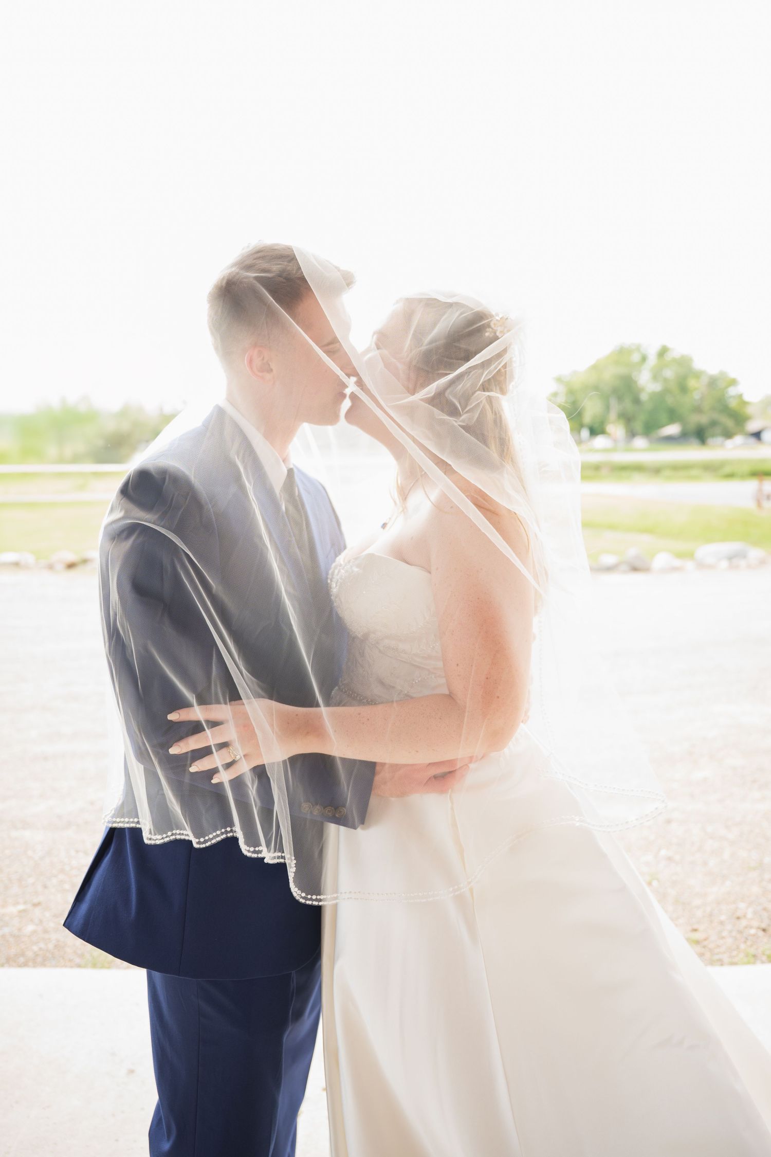 A romantic wedding moment captured in soft sunlight as a couple embraces under a delicate veil at Northern Lights near Milaca MN..