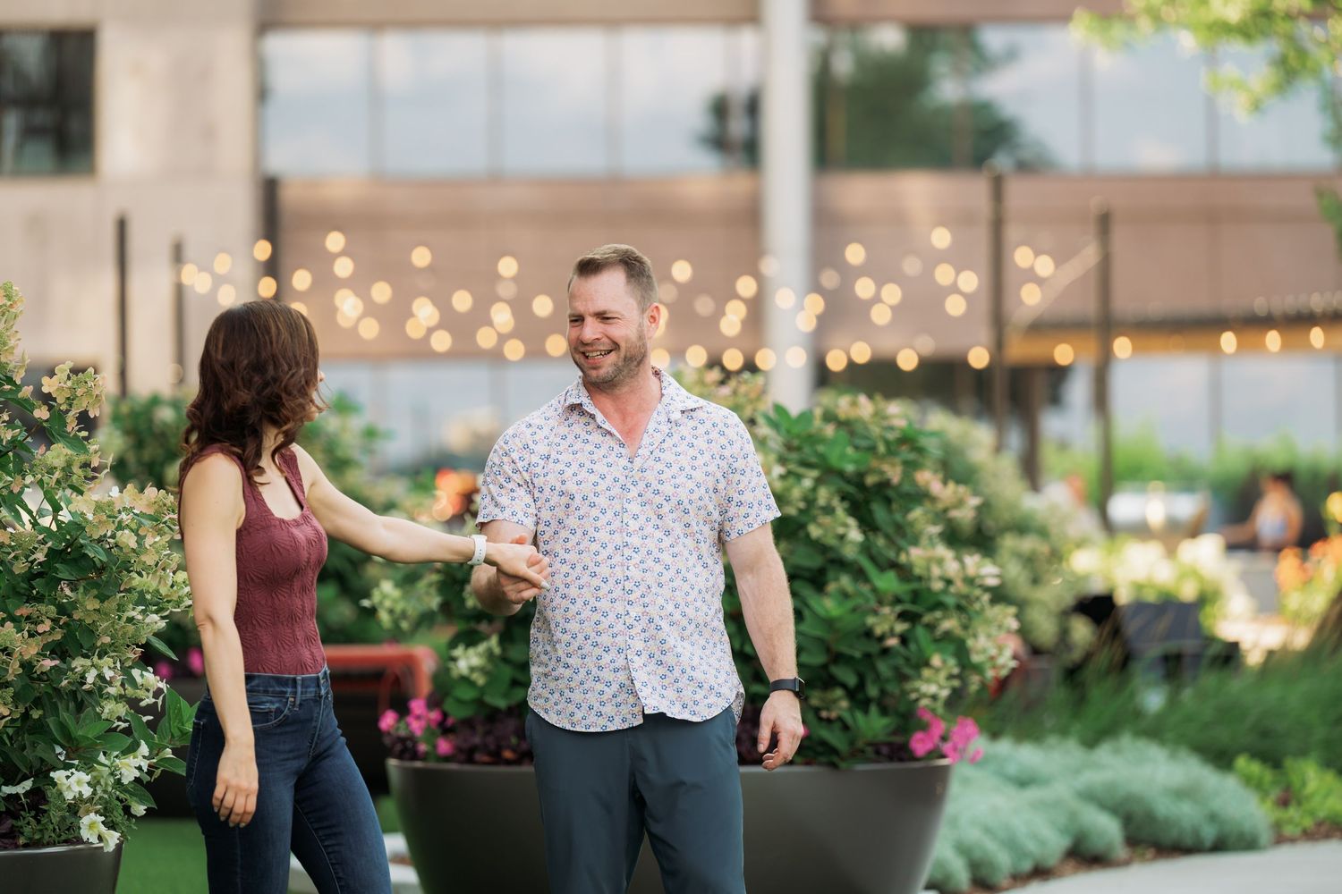 Couple dancing together on an outdoor patio with string lights and greenery in the background.