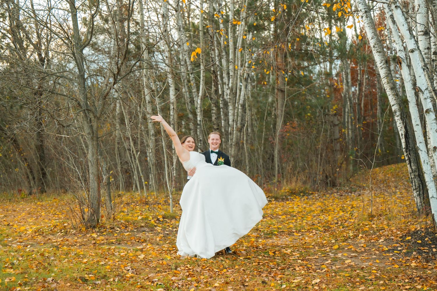 Wedding couple poses in a scenic fall forest setting with yellow leaves on the ground.