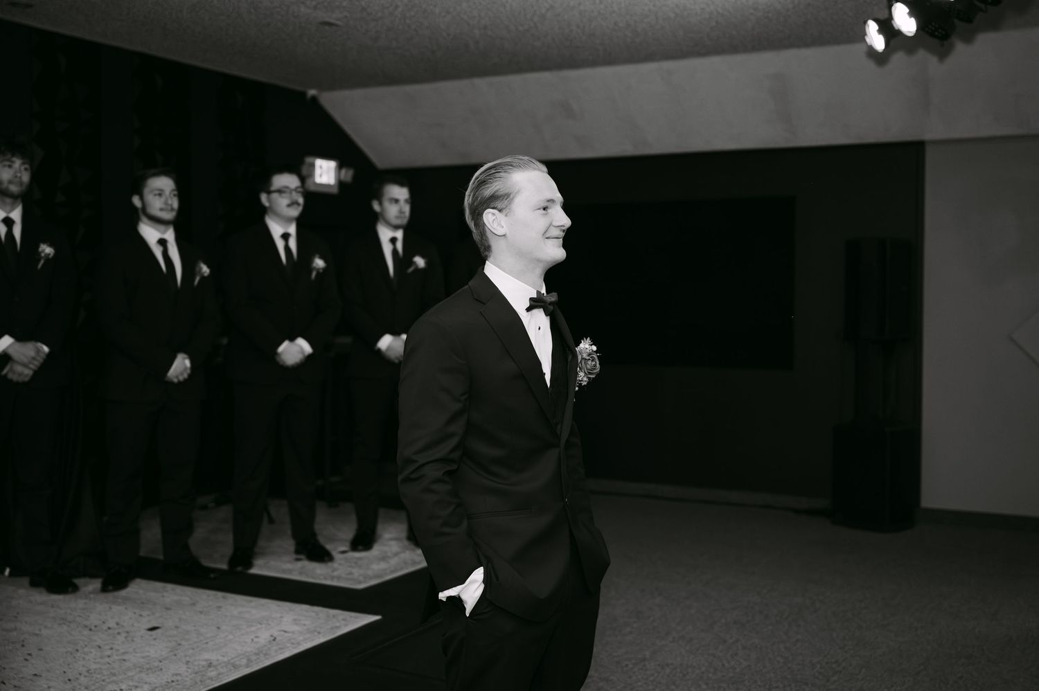 A black and white photograph shows people in formal attire walking through a dark corridor.