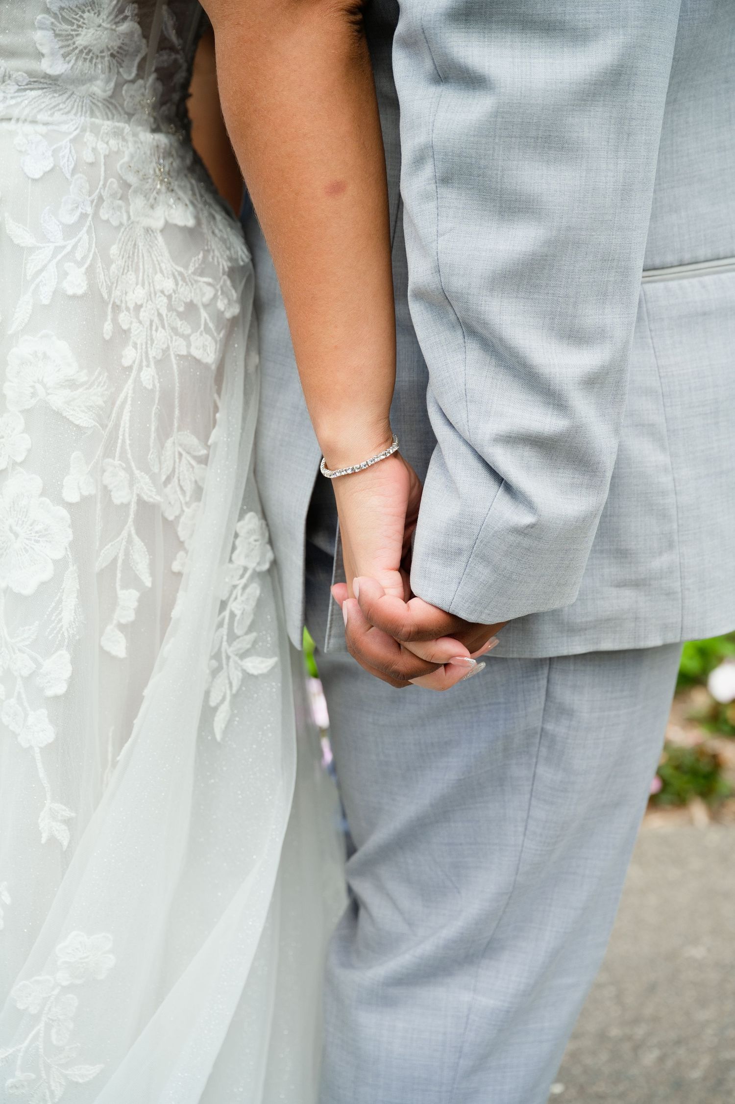 Bride and groom holding hands, bride in lace wedding dress, groom in gray suit.