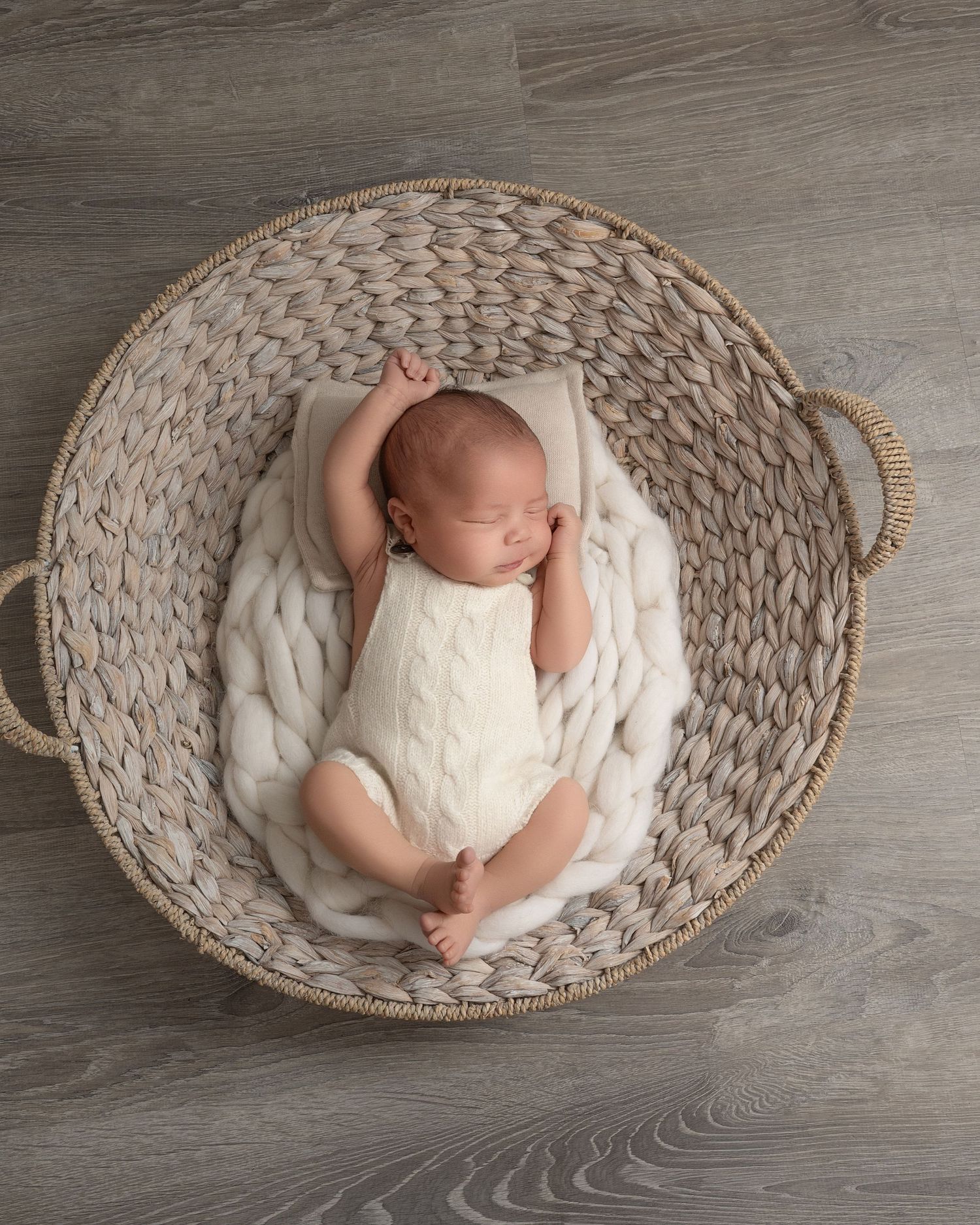 Minnesota Best newborn photographer - A newborn baby lies peacefully in a round woven basket with white blankets on a gray wooden floor.