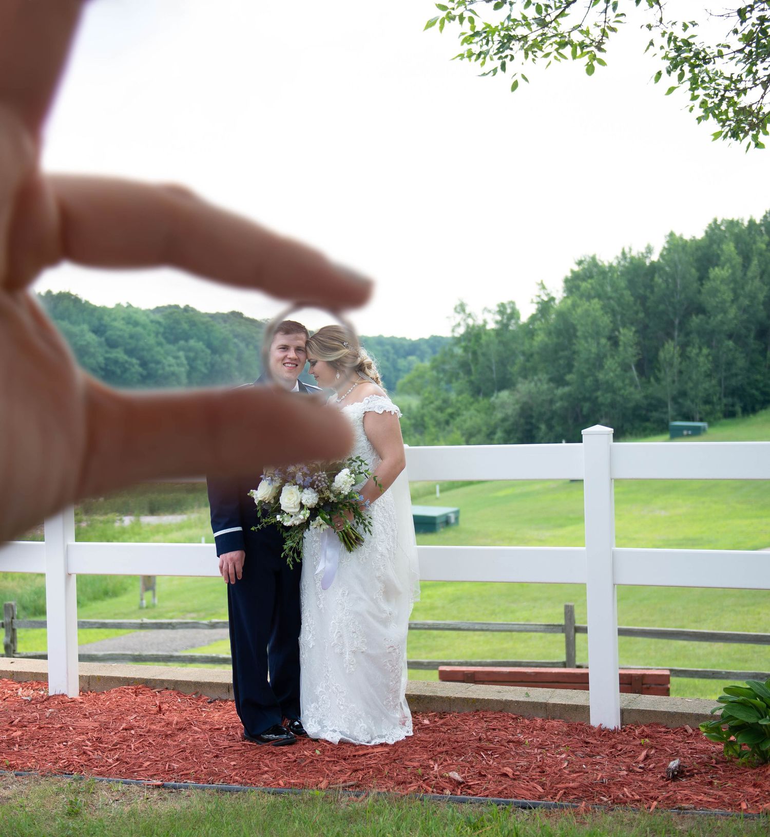 Wedding couple on red brick patio with white fence and green landscape in background. Zimmerman MN Weddings