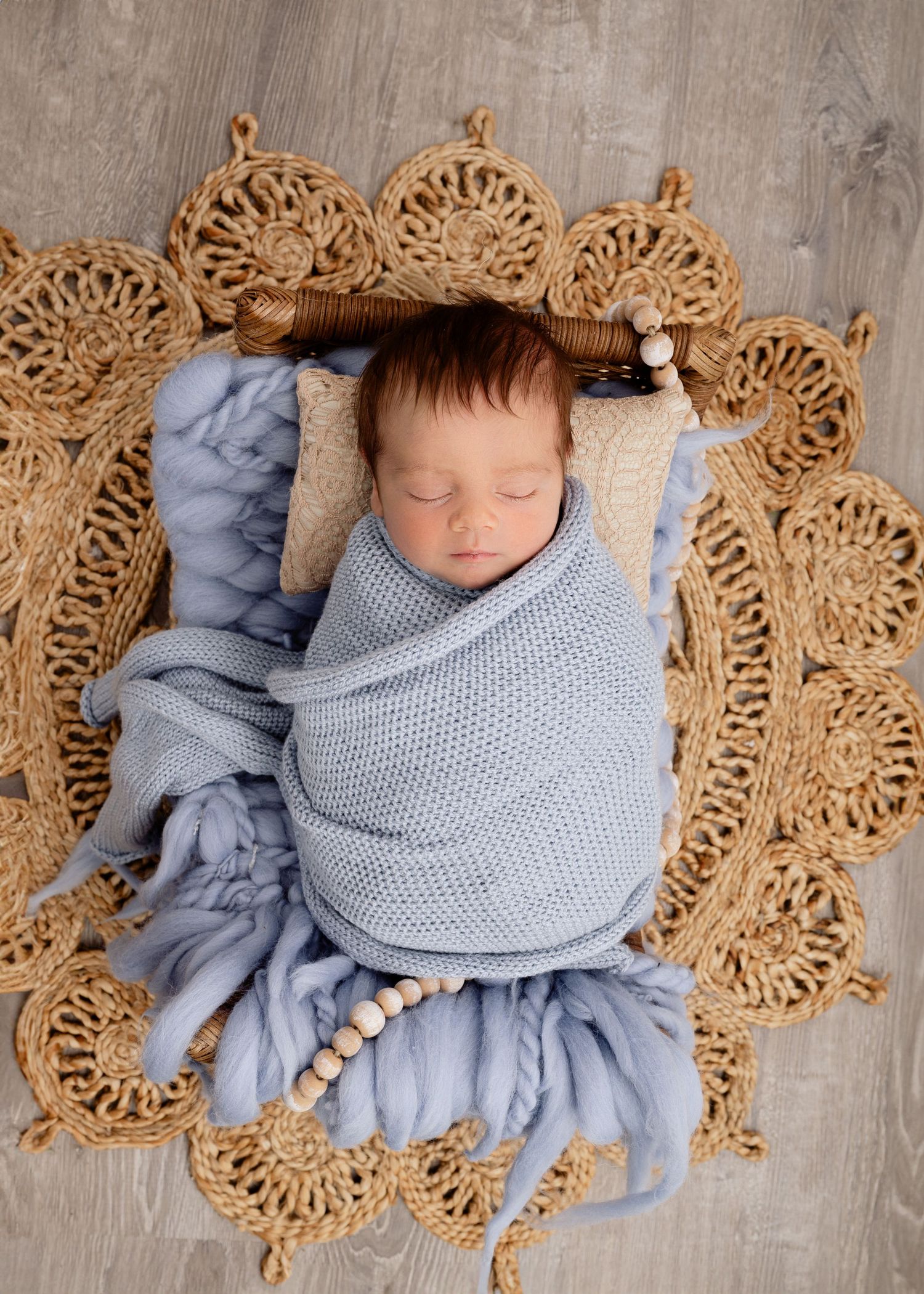 Minnesota Best newborn photos Sleeping baby wrapped in soft gray knit blanket lying on ornate woven jute circular mat with scalloped edges.