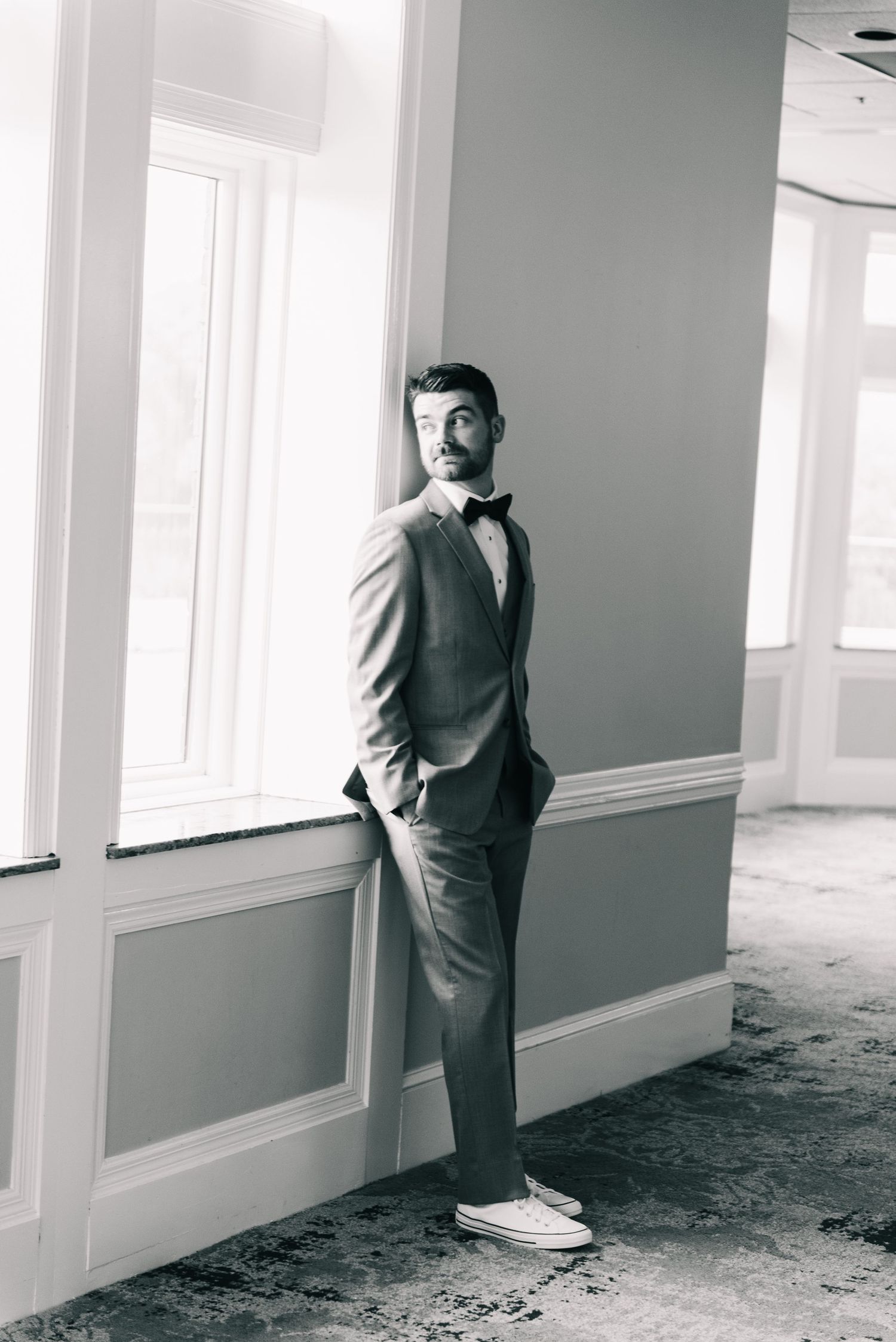 Central MN Wedding Photos | Groom in gray suit and bow tie poses by window in black and white portrait photo.