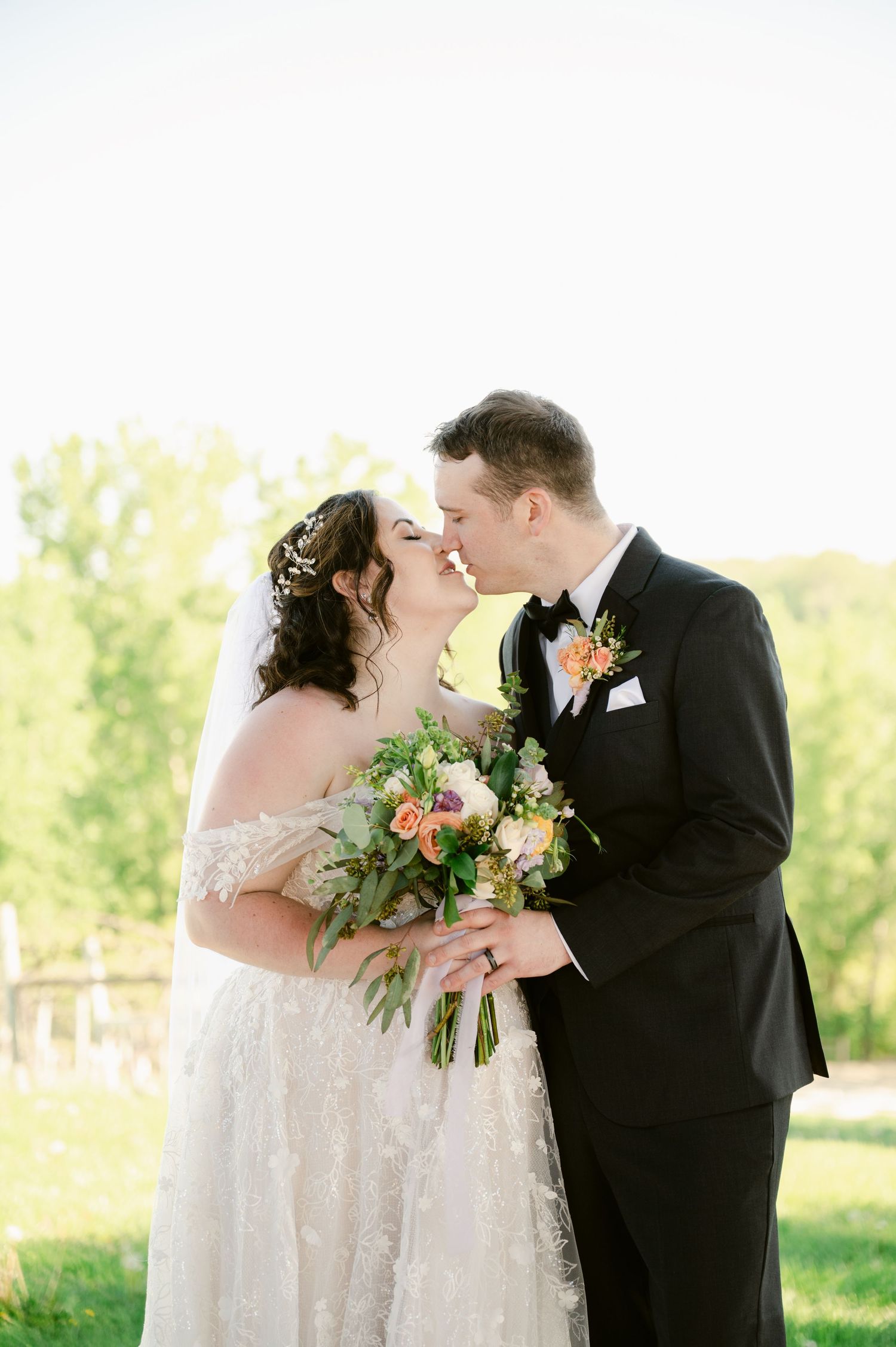 Central MN Wedding Photos - Bride and groom share a romantic almost-kiss outdoors, she holds a lush peach and green bouquet.