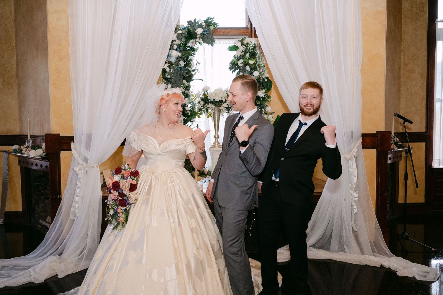 Central MN Wedding | Joyful newlyweds celebrate with officiant at floral arch altar, all three raising hands in celebration after ceremony.