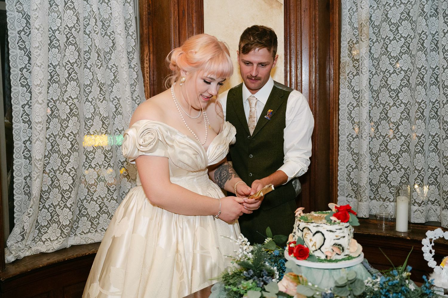 Central MN Wedding Photos | Bride and groom cut their wedding cake together in a vintage-styled venue with lace curtains.