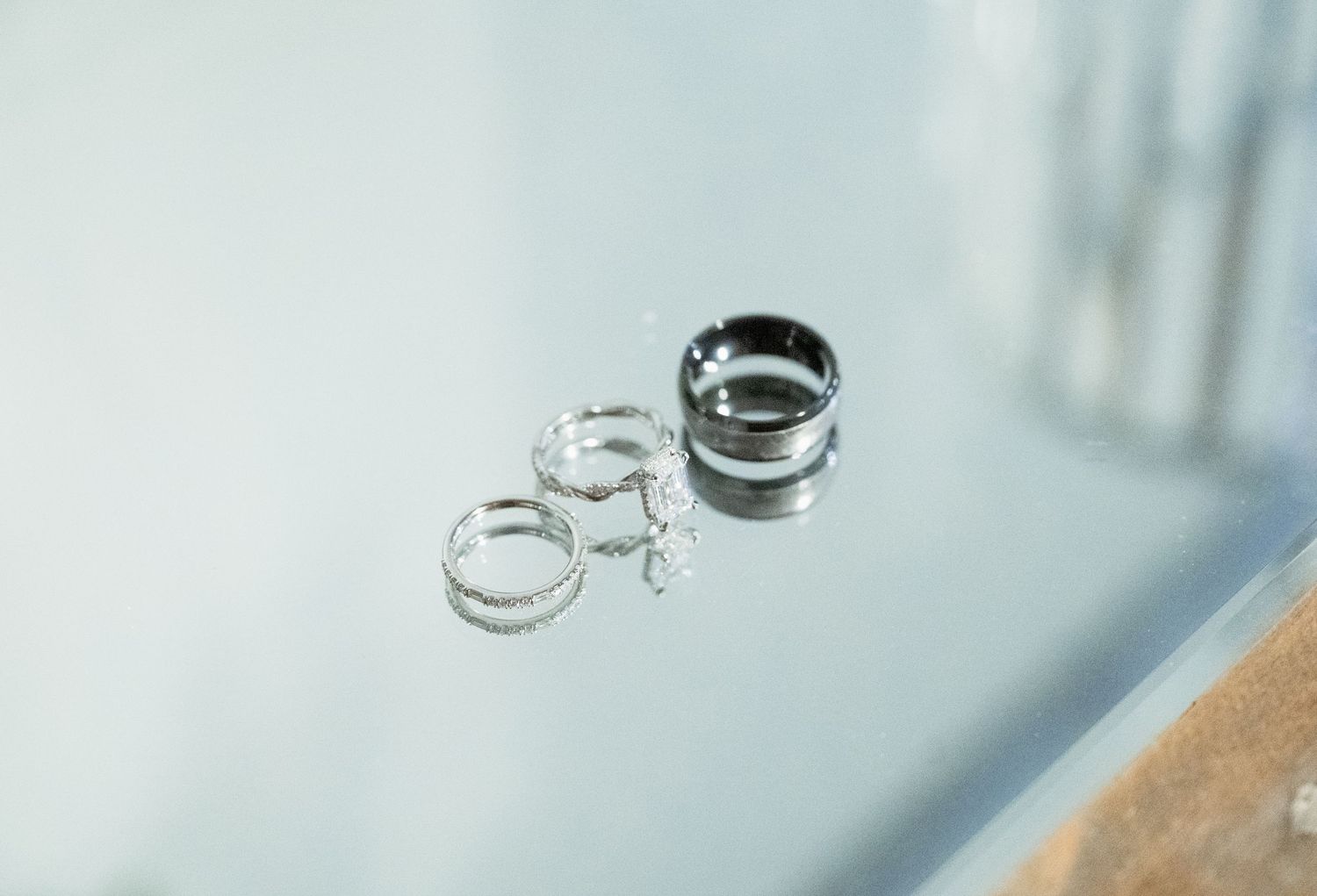 Silver wedding rings and bands arranged on a reflective glass surface, including a wide band and delicate hoop rings.