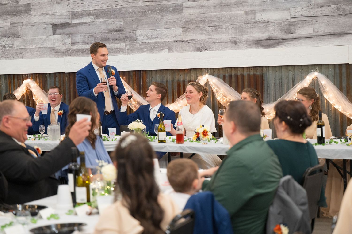 Wedding guests enjoying a casual outdoor reception at long tables with drinks and conversation.