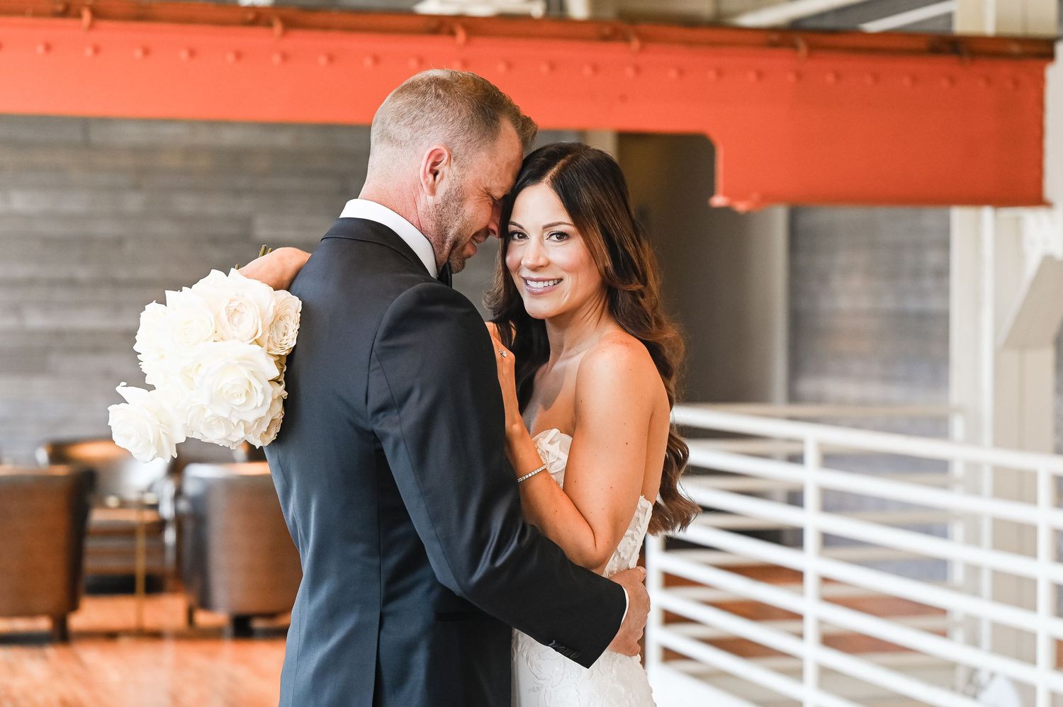 First look wedding photos captured in an industrial venue with red accent walls and natural light.