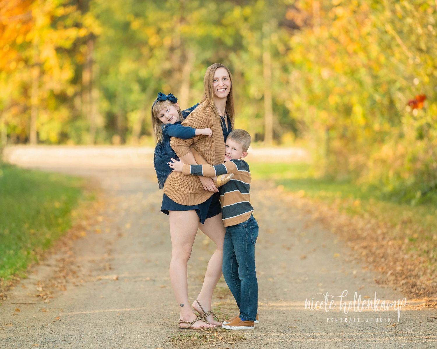 A couple embraces on a tree-lined path with golden autumn foliage creating a romantic fall backdrop.