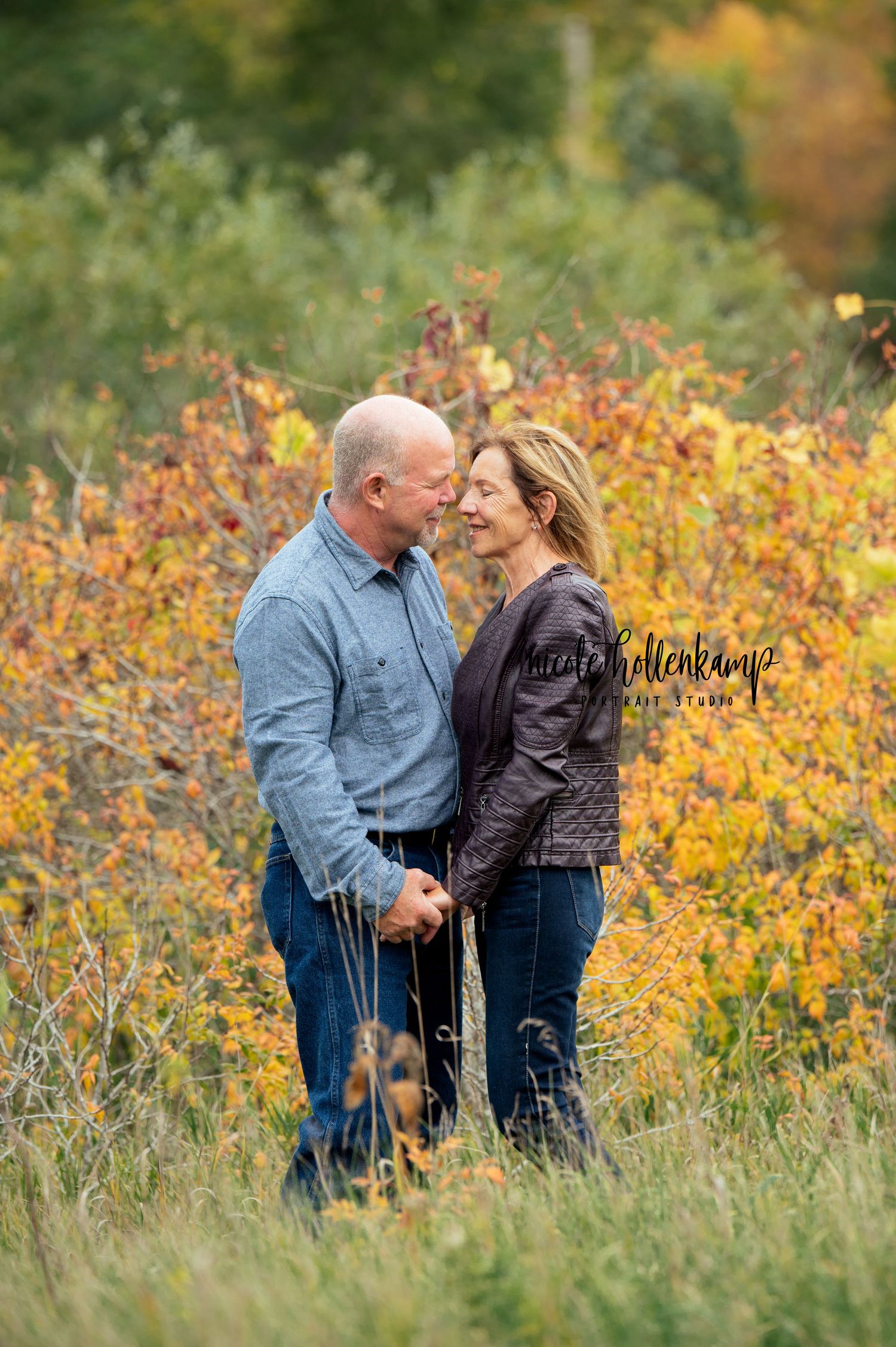 Romantic couple embraces while standing in field of golden fall foliage.