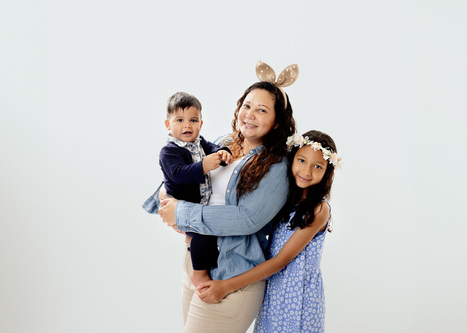 A playful studio portrait of a mother and two children wearing casual outfits.