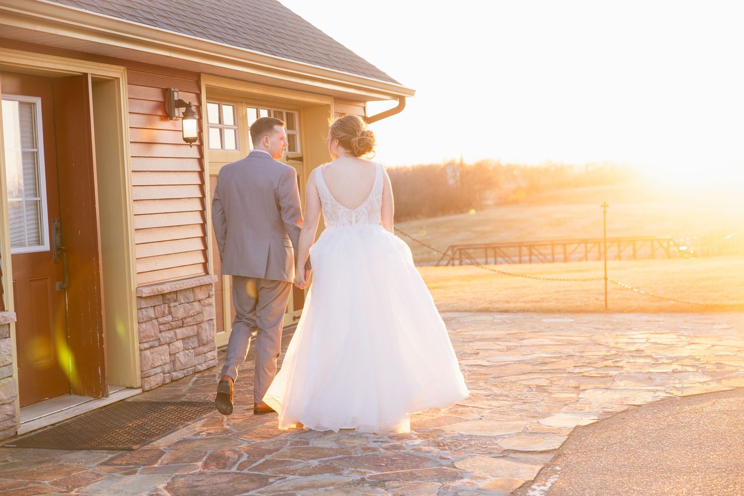 Bride and groom walk hand-in-hand toward a building bathed in golden sunset light.