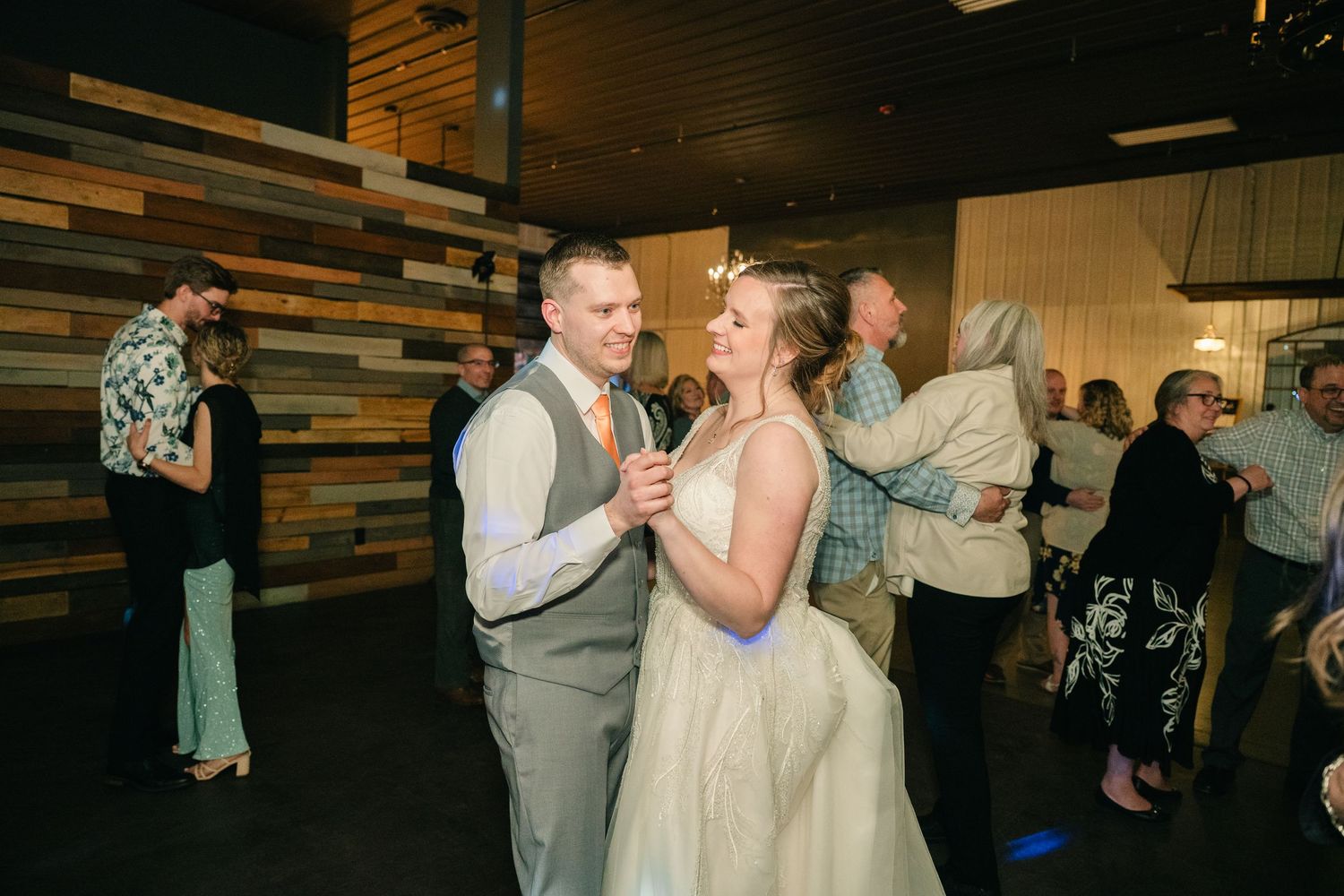 Bride and groom share a dance surrounded by guests on the dance floor at wedding reception.
