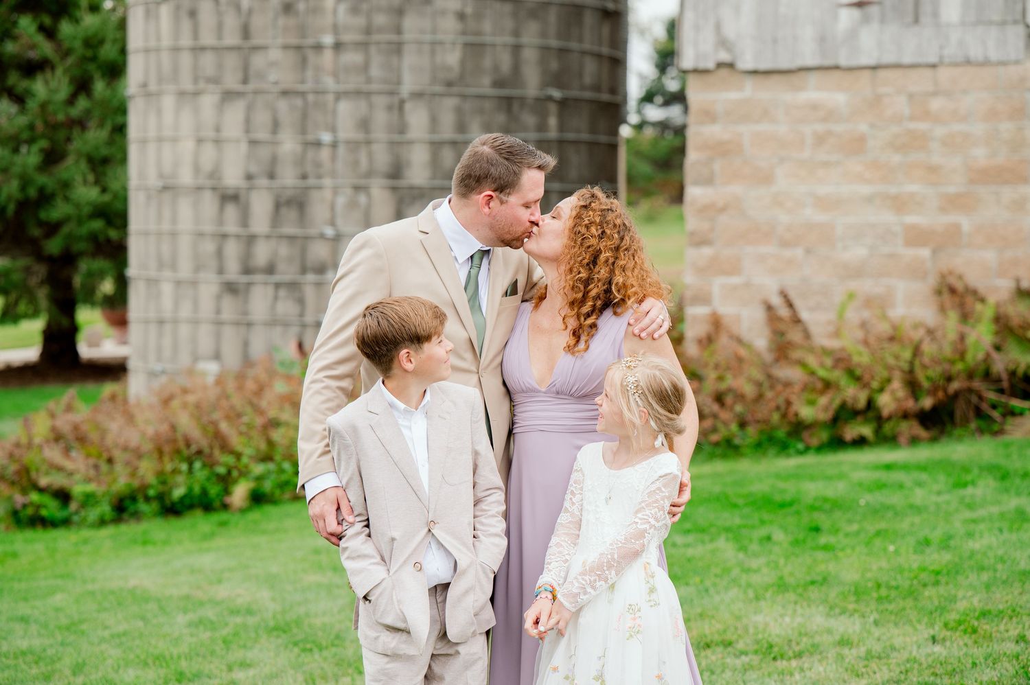 Family portrait with children in formal attire at outdoor rustic wedding setting.