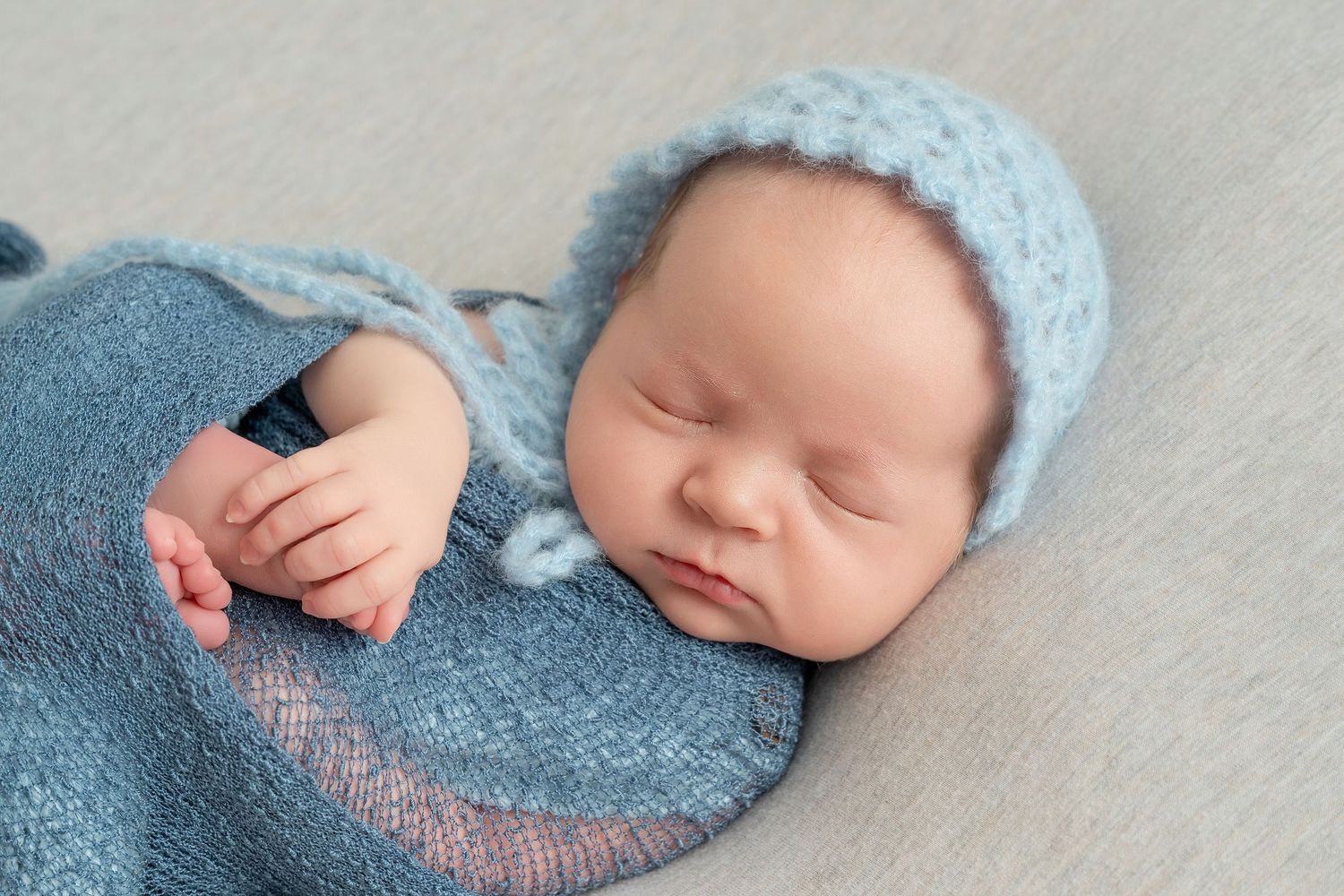 Minnesota Best newborn photographer -  a Sleeping newborn in blue knit clothing lying on soft gray backdrop.